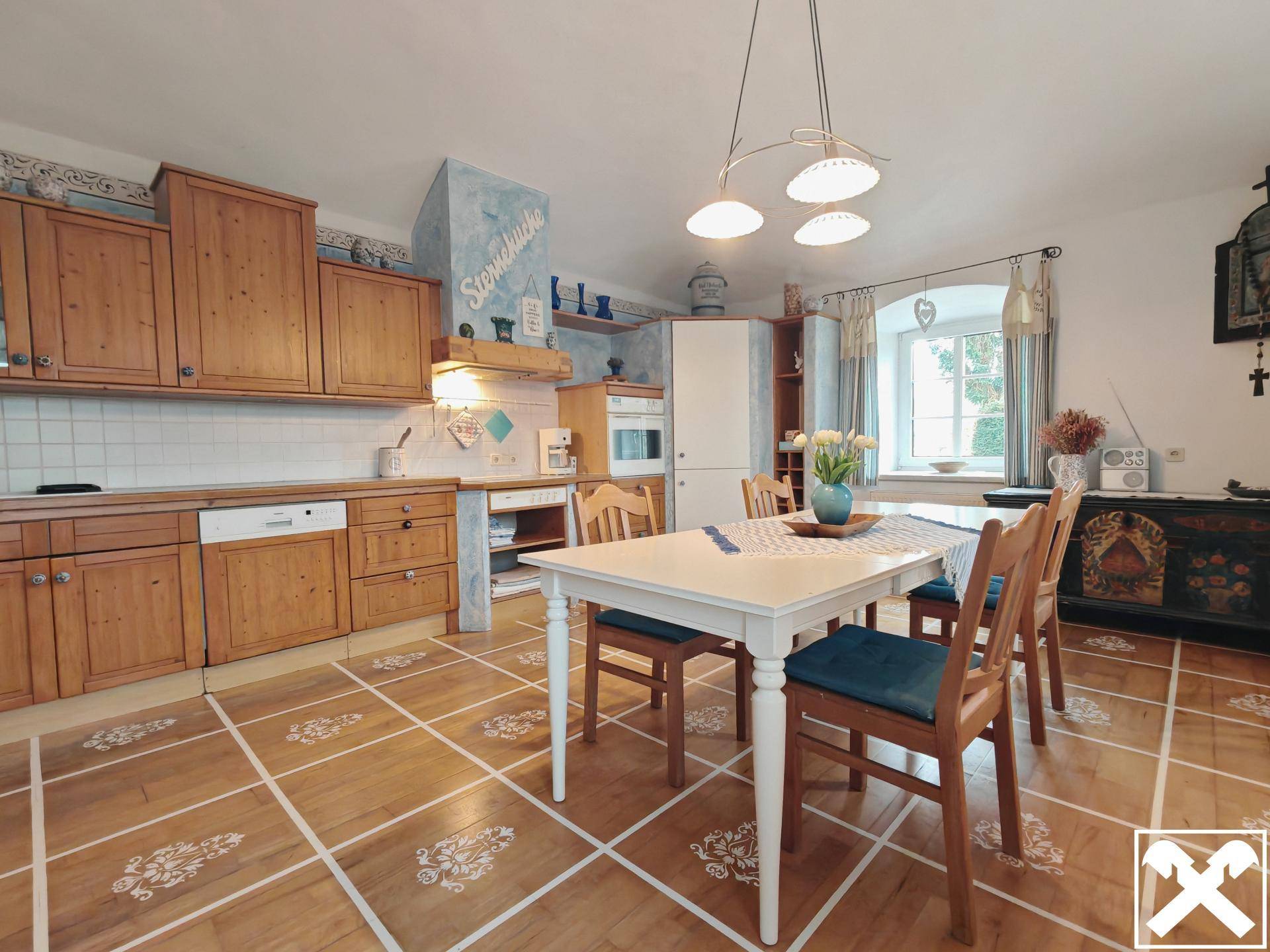 Geräumige Wohnküche mit Holzeinbauten, Esstisch und Fenster mit Blick ins Grüne.