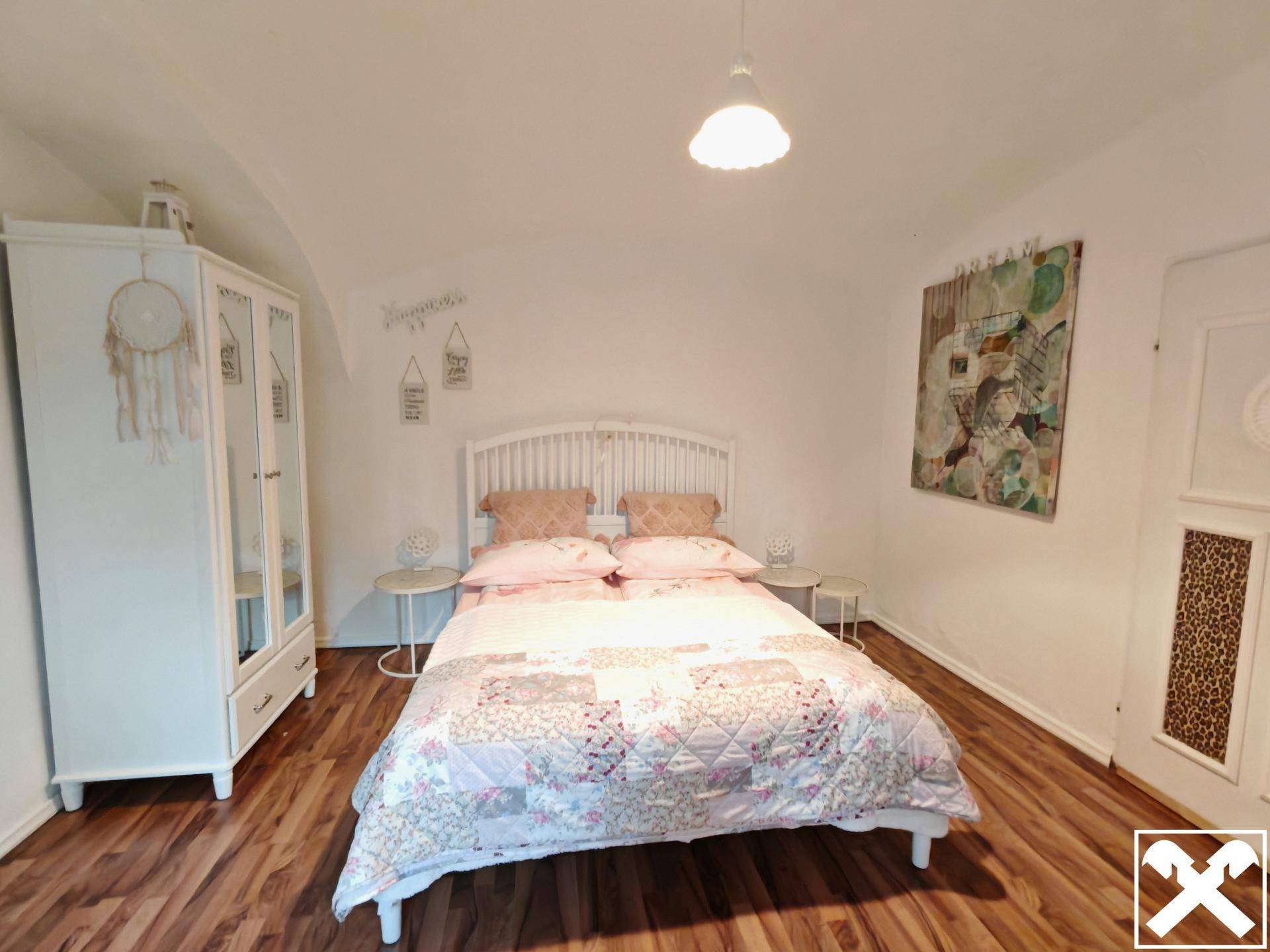 Helles Schlafzimmer mit Holzboden, weißem Bett und Kleiderschrank in freundlicher Atmosphäre.