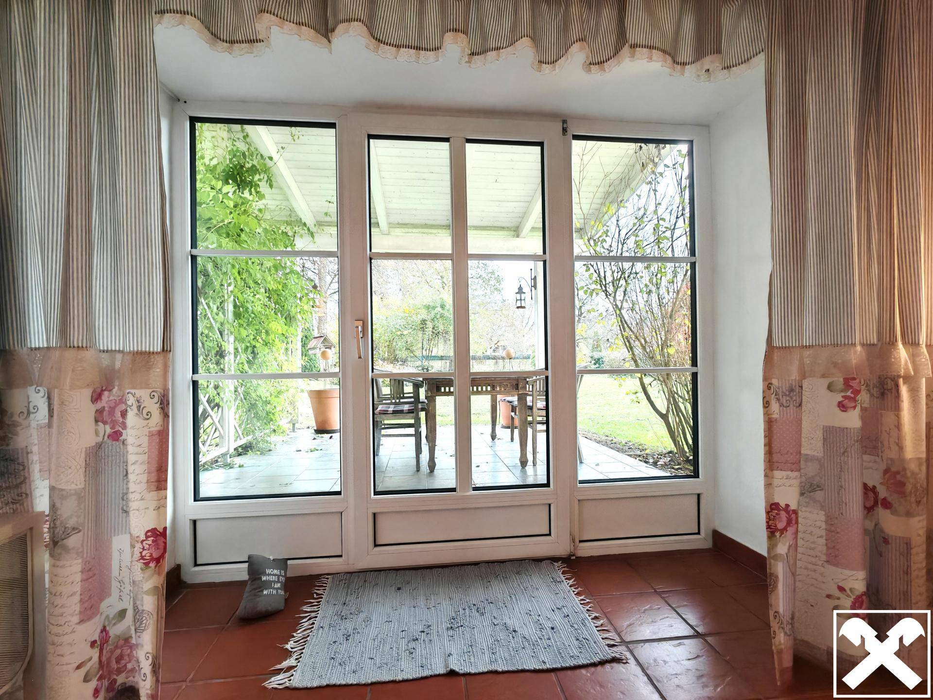 Heller Wintergarten mit großen Fenstern und Blick auf den Außenbereich mit Sitzgelegenheiten.