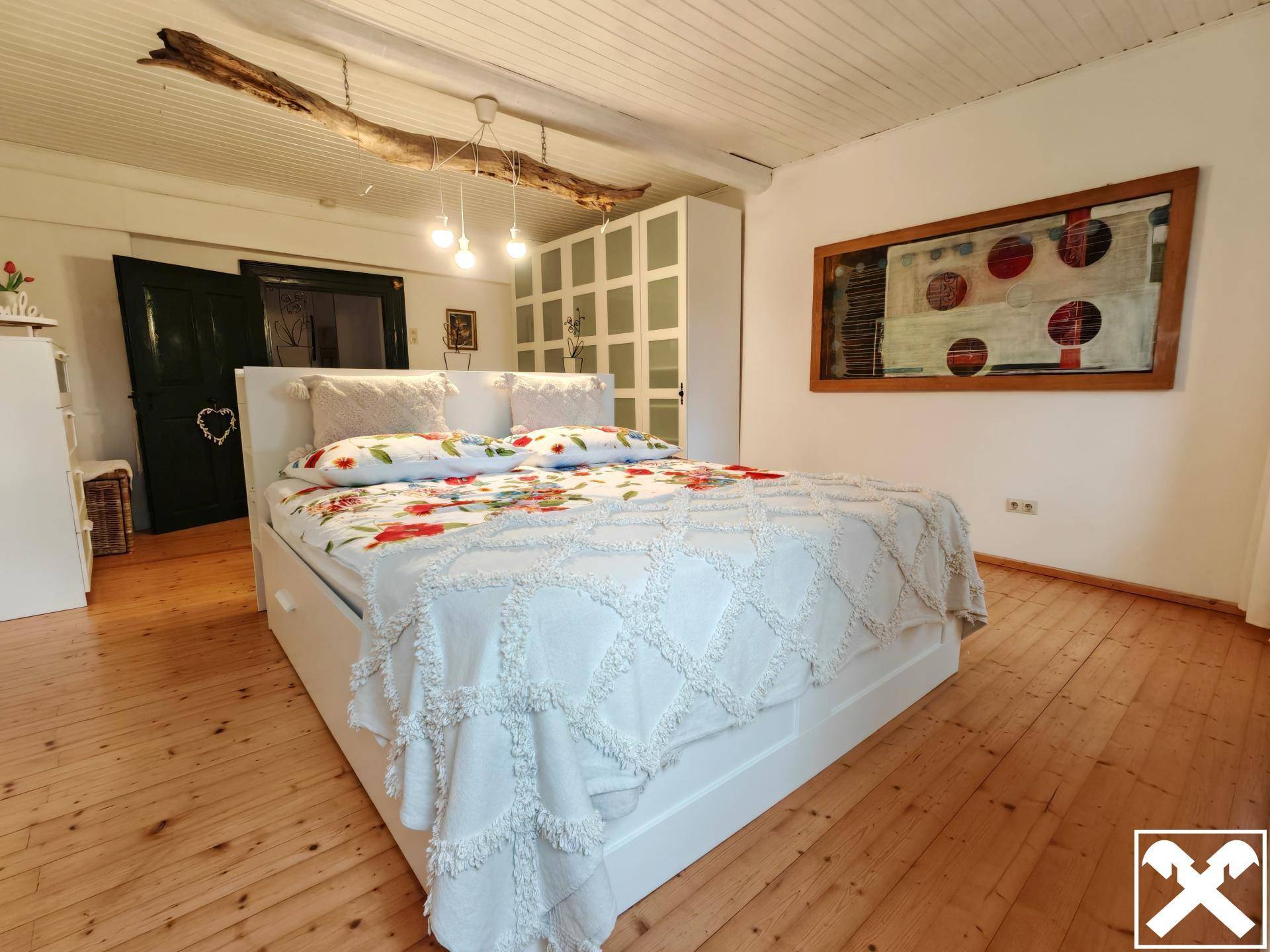 Helles Schlafzimmer mit Holzdielenboden, weißem Bett und Schrank in ländlichem Stil.