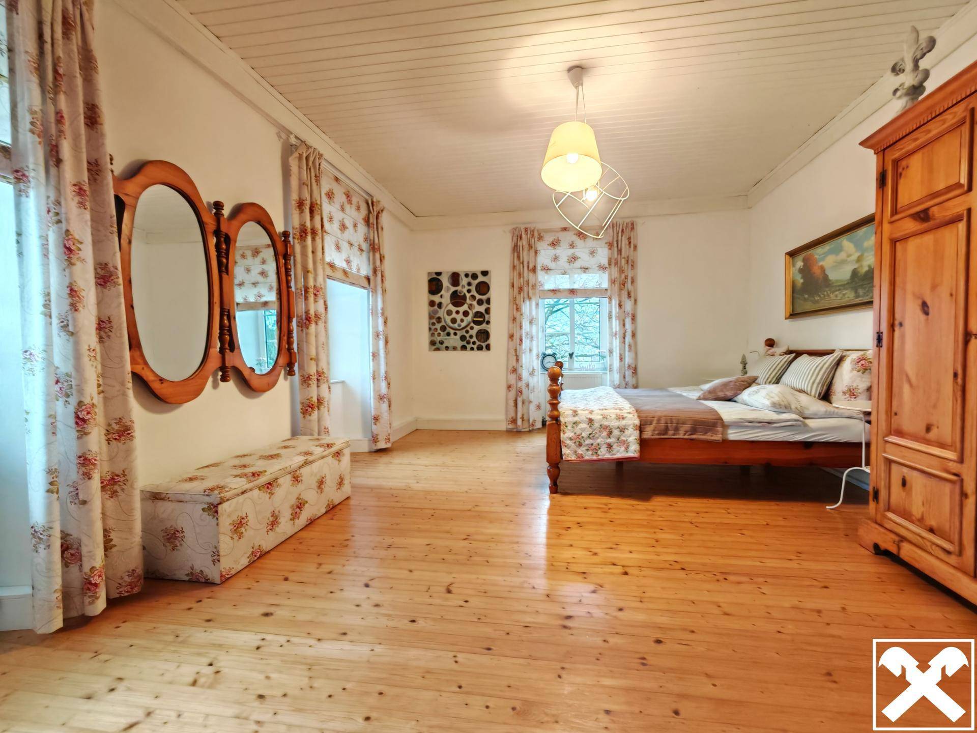 Großes Schlafzimmer mit Holzdielenboden, zwei Fenstern und traditionellen Holzmöbeln.