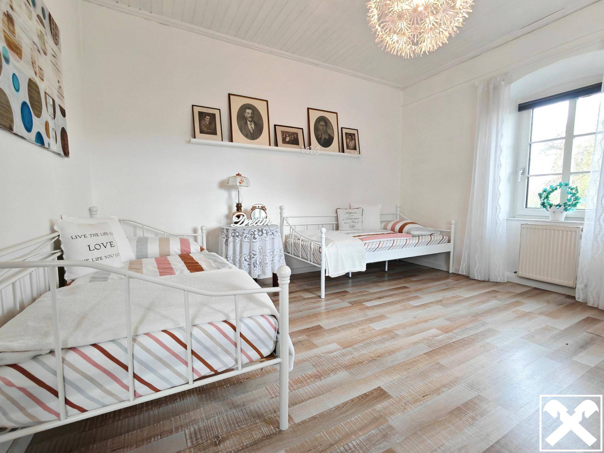 Helles Schlafzimmer mit zwei Einzelbetten, Holzboden und Fenster mit Tageslicht.