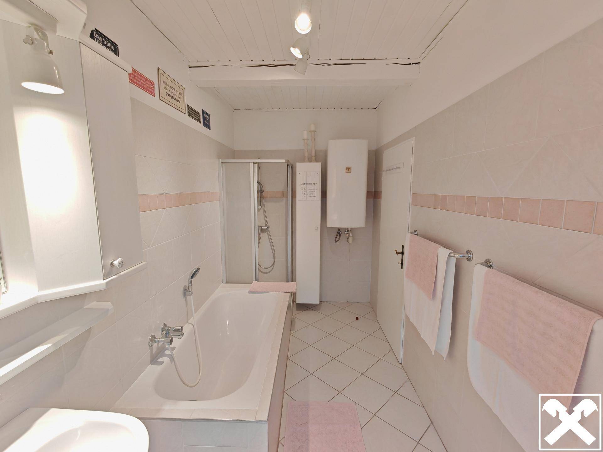 Badezimmer mit Badewanne, Duschkabine und hellen Fliesen in Rosa- und Weißtönen.