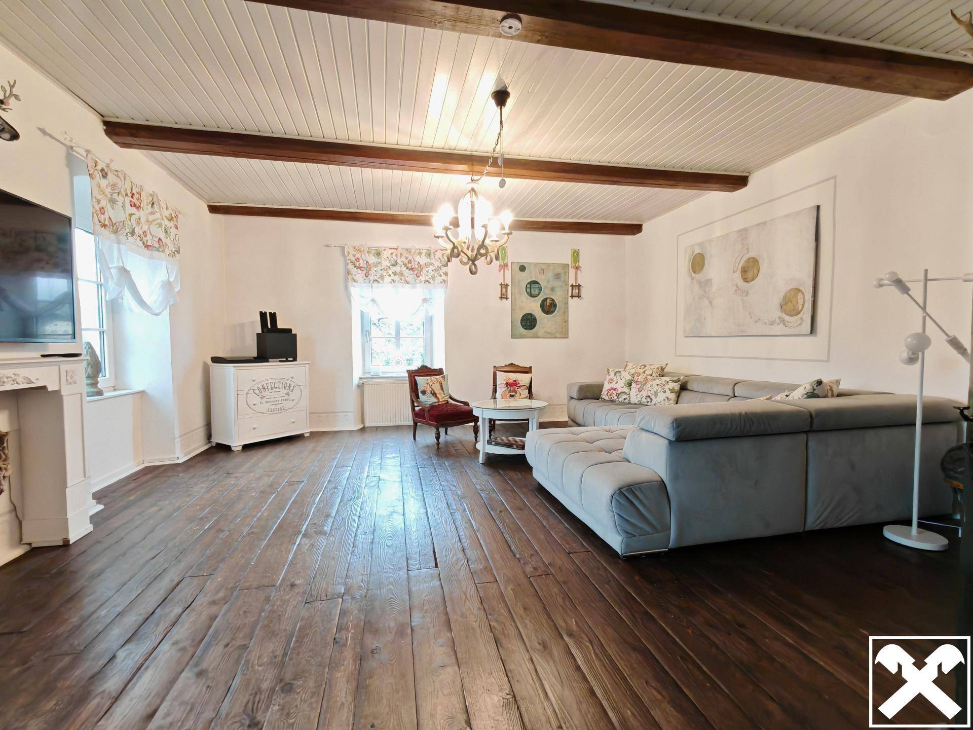 Geräumiges Wohnzimmer mit Holzbalkendecke, Dielenboden und gemütlicher Sitzecke.