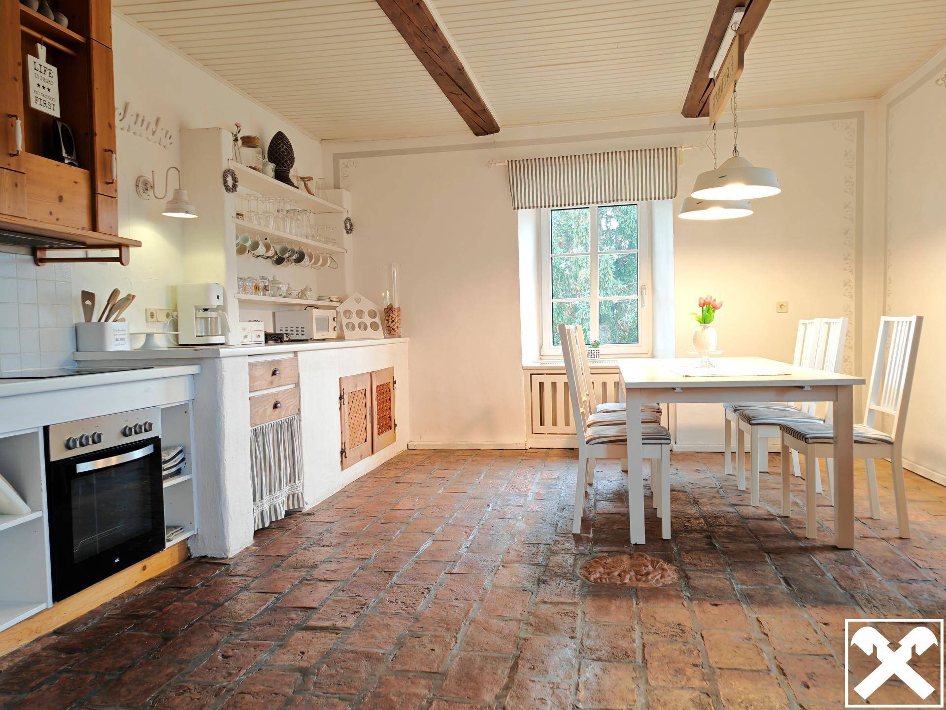 Rustikale Küche mit Backsteinboden, Holzelementen und Essbereich am Fenster.