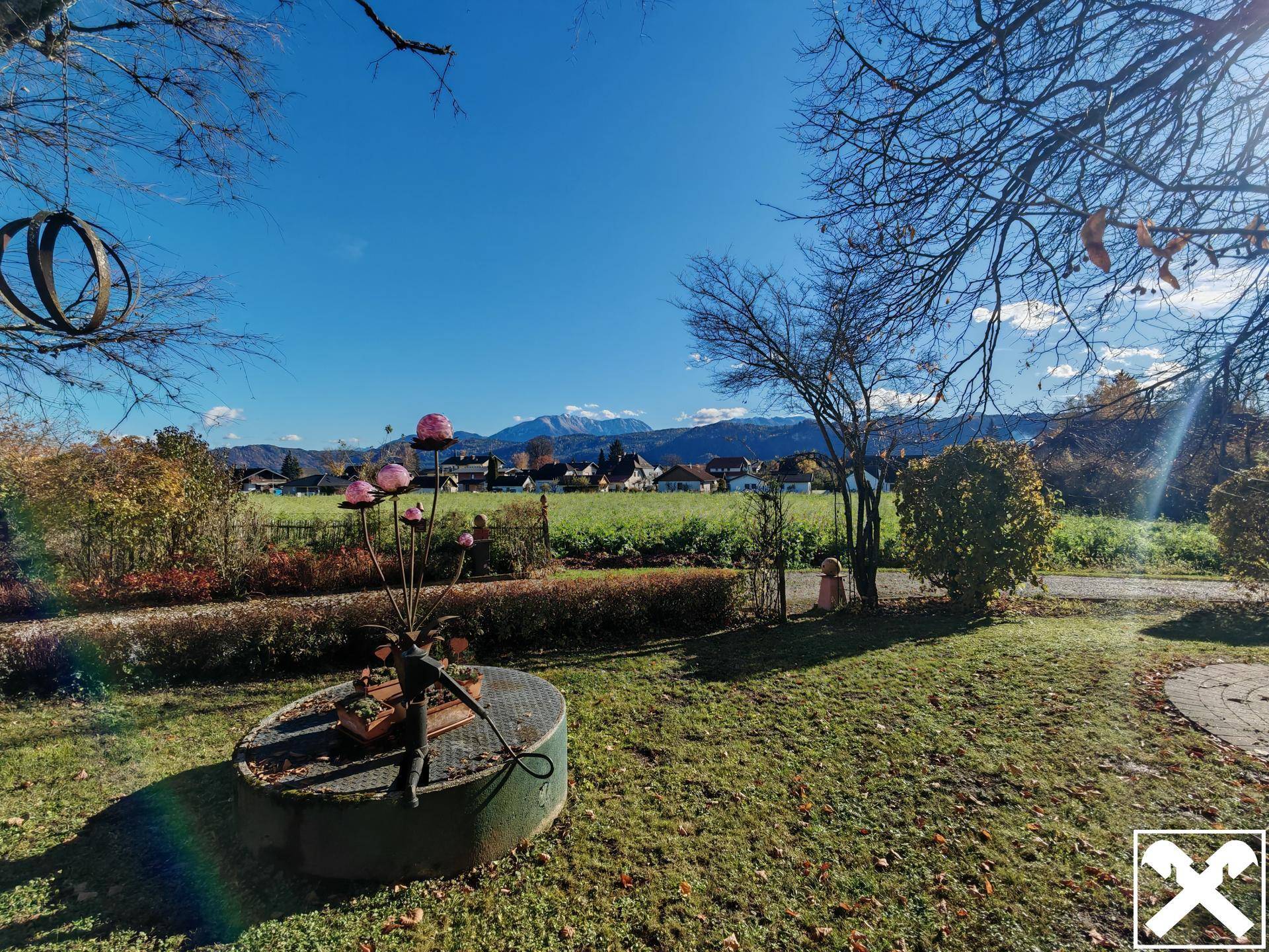 Sonniger Garten mit einem alten Brunnen, Rasenfläche und weitem Blick auf die Berge.