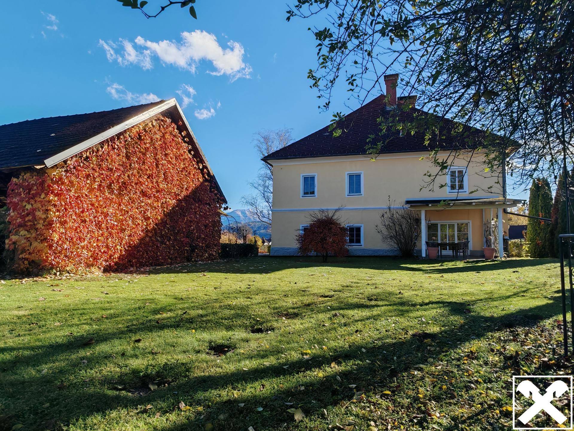 Rückseite des Hauses mit großer Rasenfläche und einem Nebengebäude mit Herbstlaub.