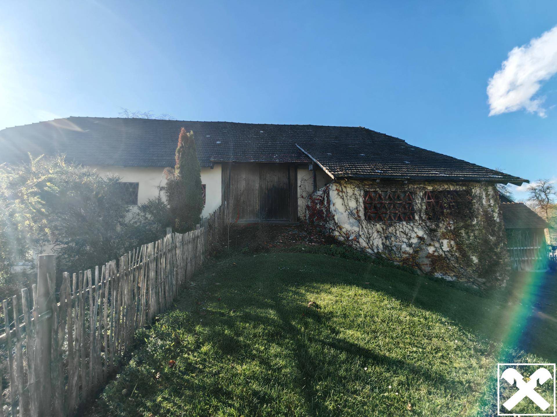 Seitenansicht eines alten Holzgebäudes mit Zaun und Bewuchs.