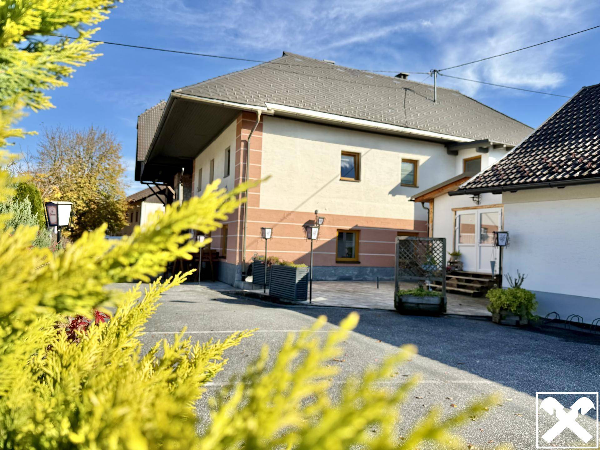 Gebäudeansicht aus der Ferne, teilweise verdeckt von herbstlichem Laub und Sträuchern, die eine malerische Kulisse bilden.