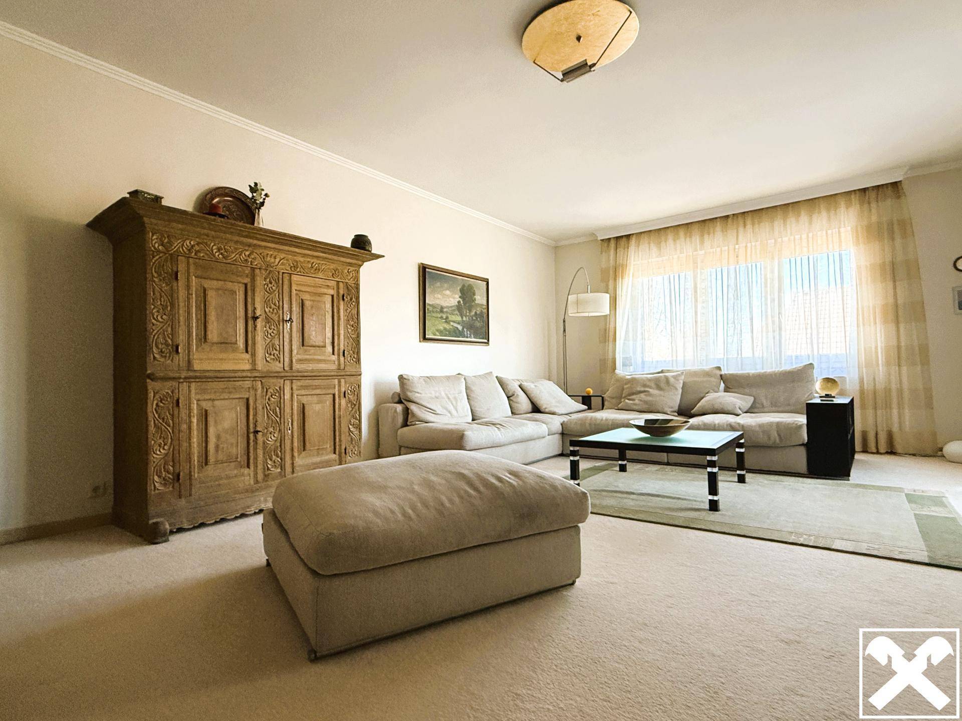 Gemütliches Wohnzimmer mit Teppichboden, beigem Sofa und einem antiken Holzschrank.
