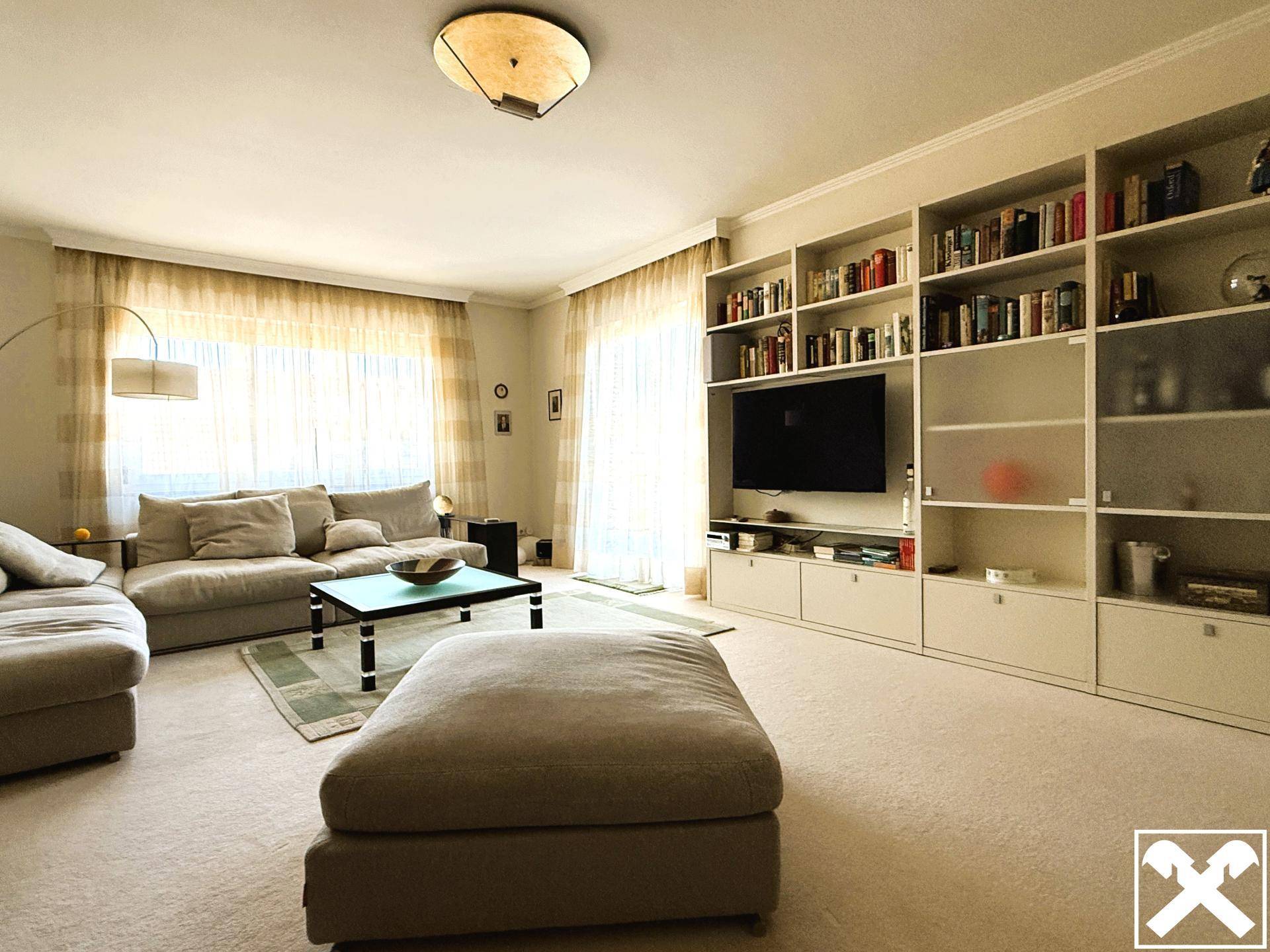 Wohnzimmer mit großem Sofa, Teppichboden und einer umfangreichen Bücherwand mit integriertem TV.