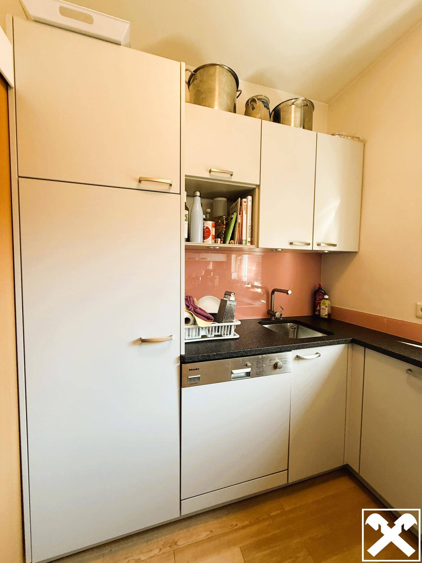 Kleine Küche mit weißen Schränken, Spülmaschine und pinkfarbener Rückwand.