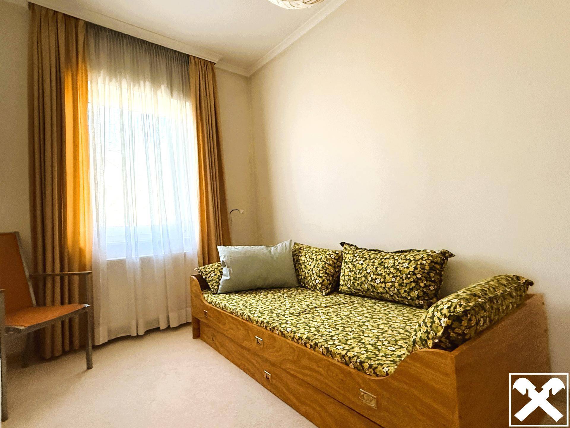 Helles Schlafzimmer mit Tagesbett, Teppichboden und großen Fenstern.