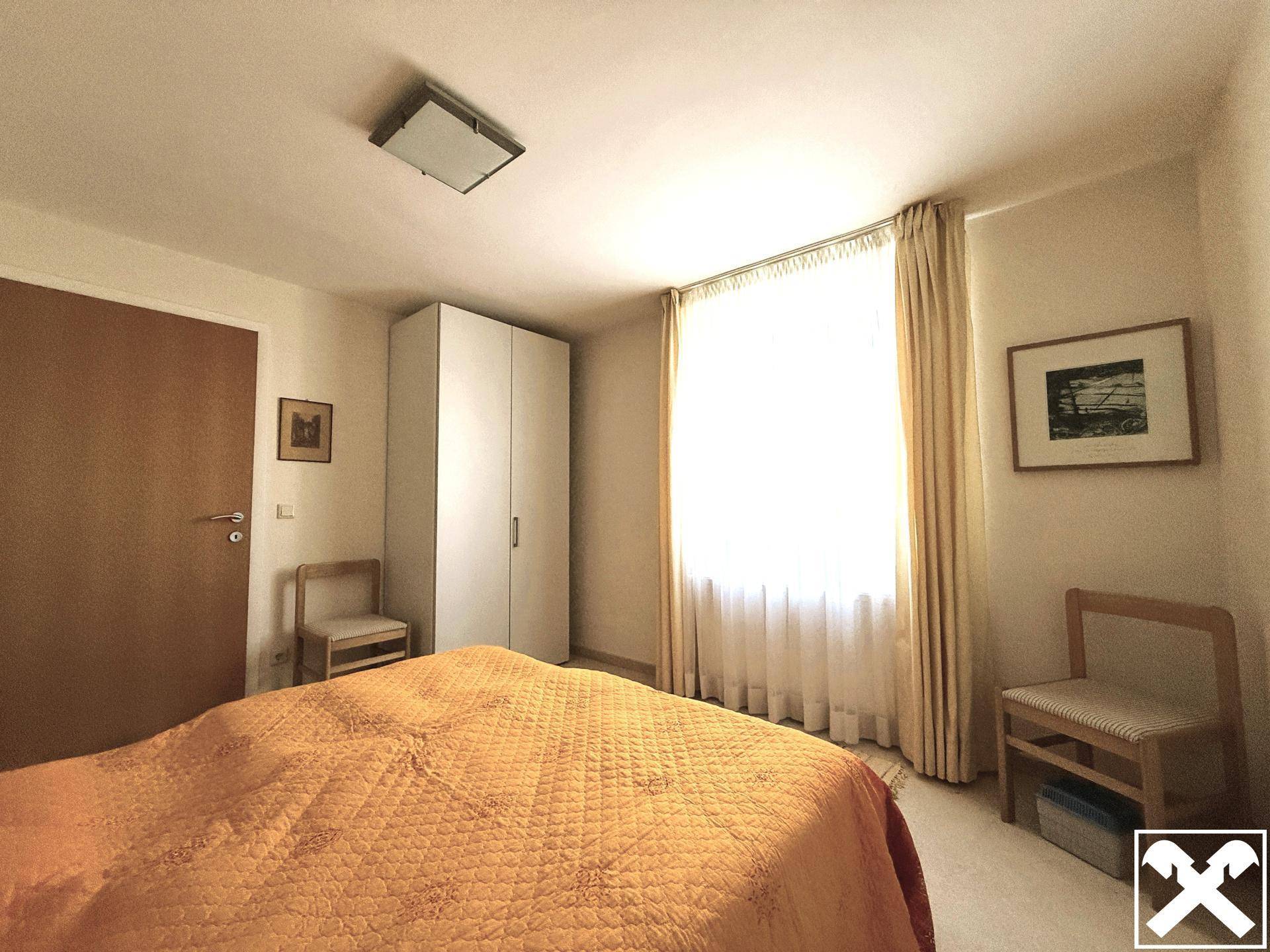 Schlafzimmer mit Doppelbett, weißem Kleiderschrank und hellem Fenster.