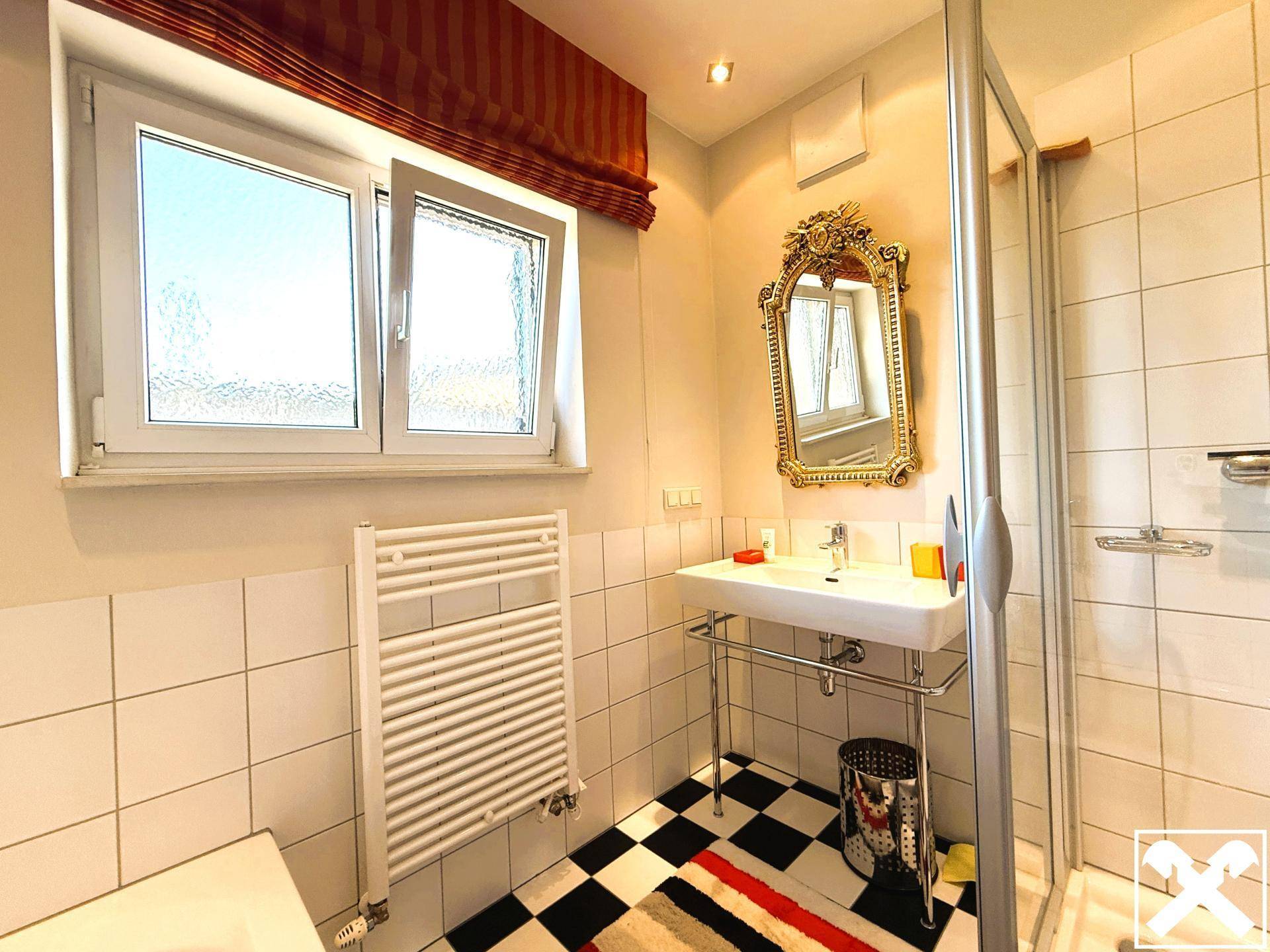 Badezimmer mit Dusche, Waschbecken, Fenster und schwarz-weißem Fliesenboden.