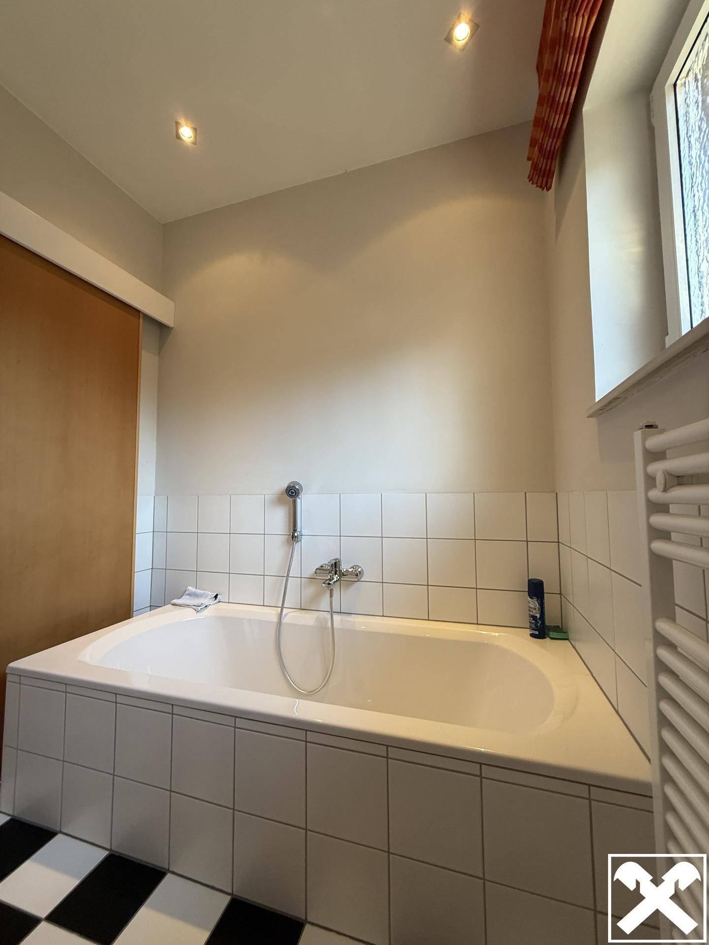 Badezimmer mit eingebauter Badewanne, weißen Fliesen und schwarz-weißem Fliesenboden.