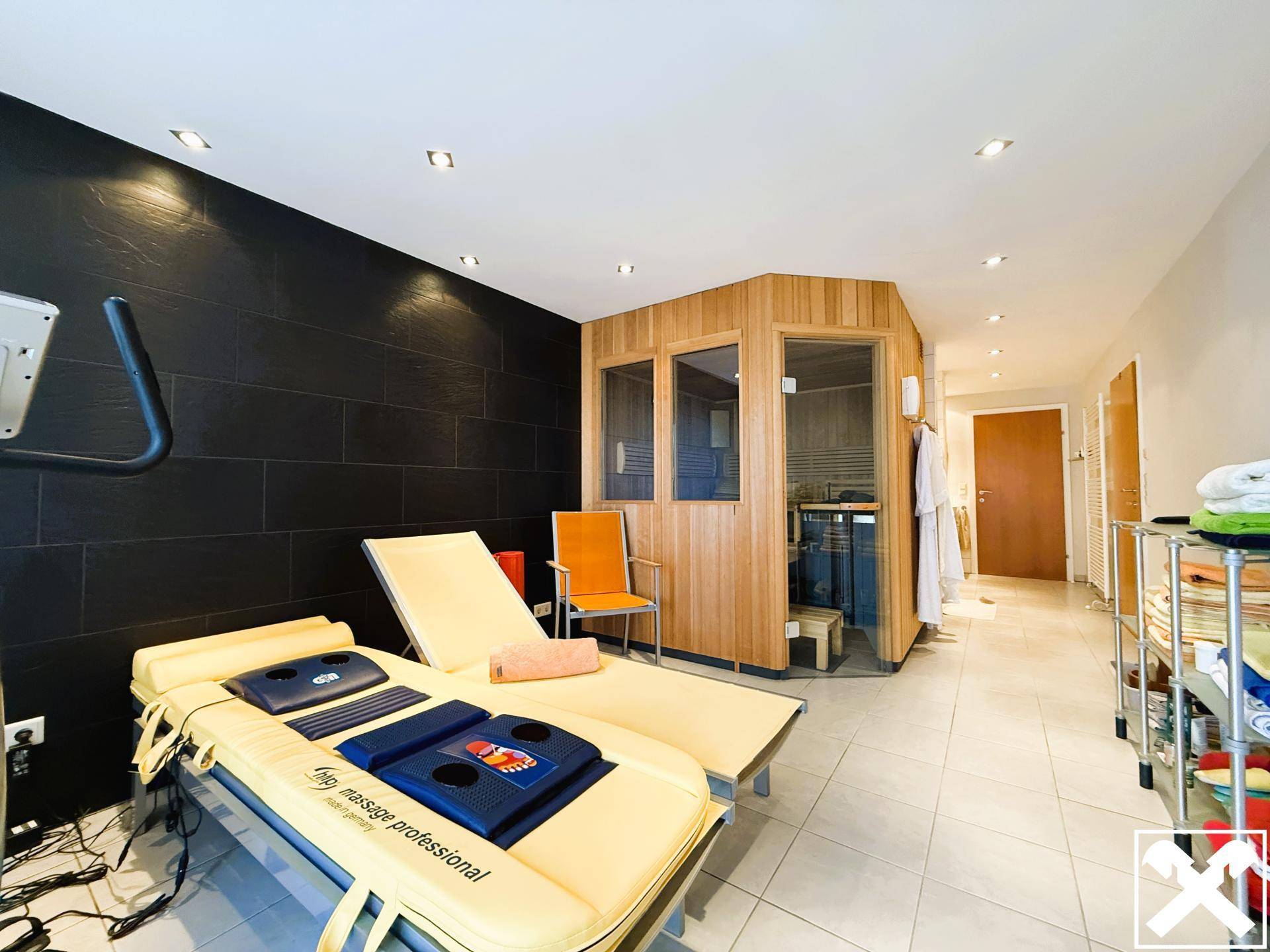 Geräumiger Wellnessbereich mit Sauna, Massageliege und Fitnessgerät für Entspannung und Training.