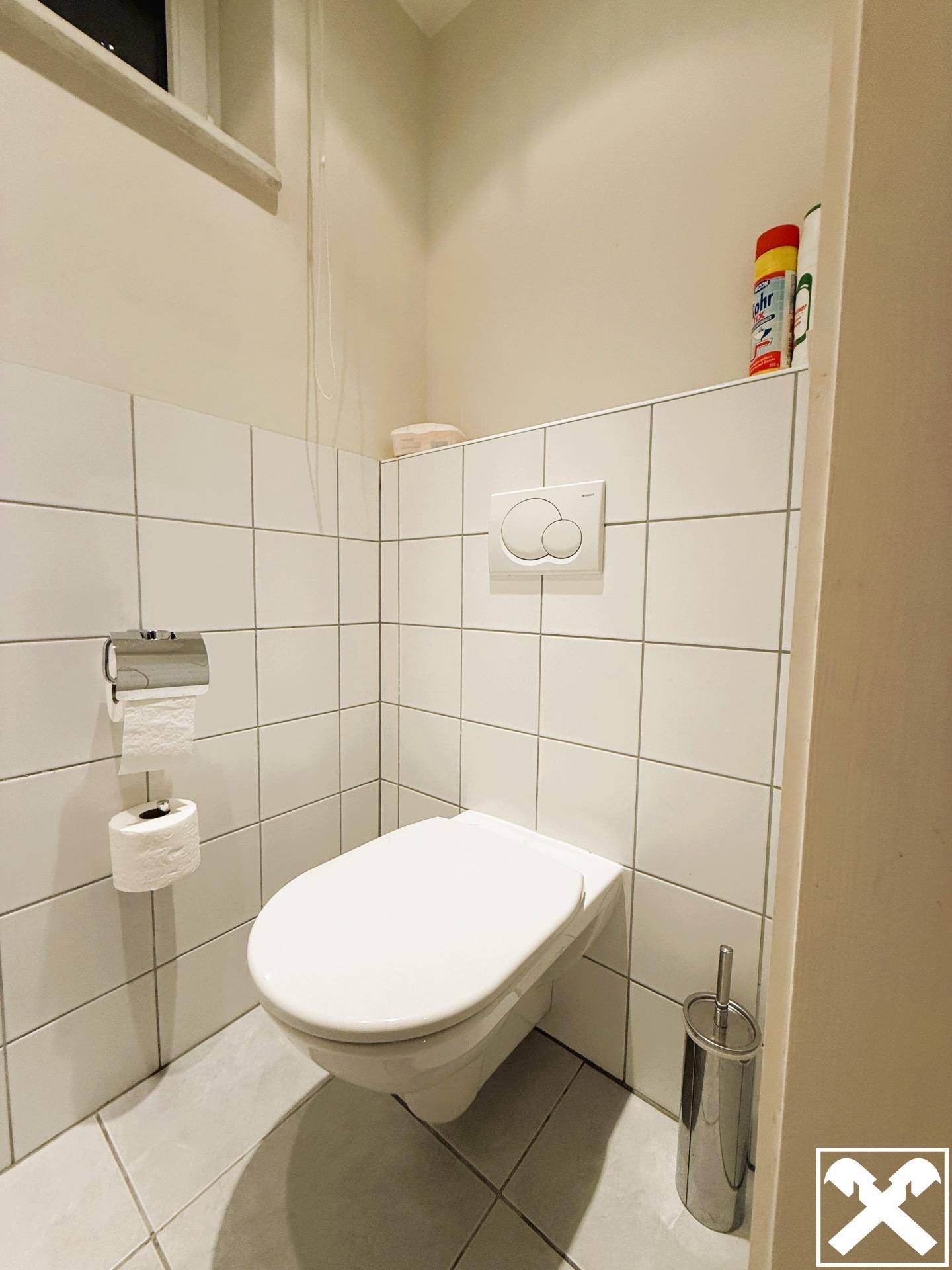 Kompaktes Gäste-WC mit wandhängender Toilette und weißen Fliesen an den Wänden.