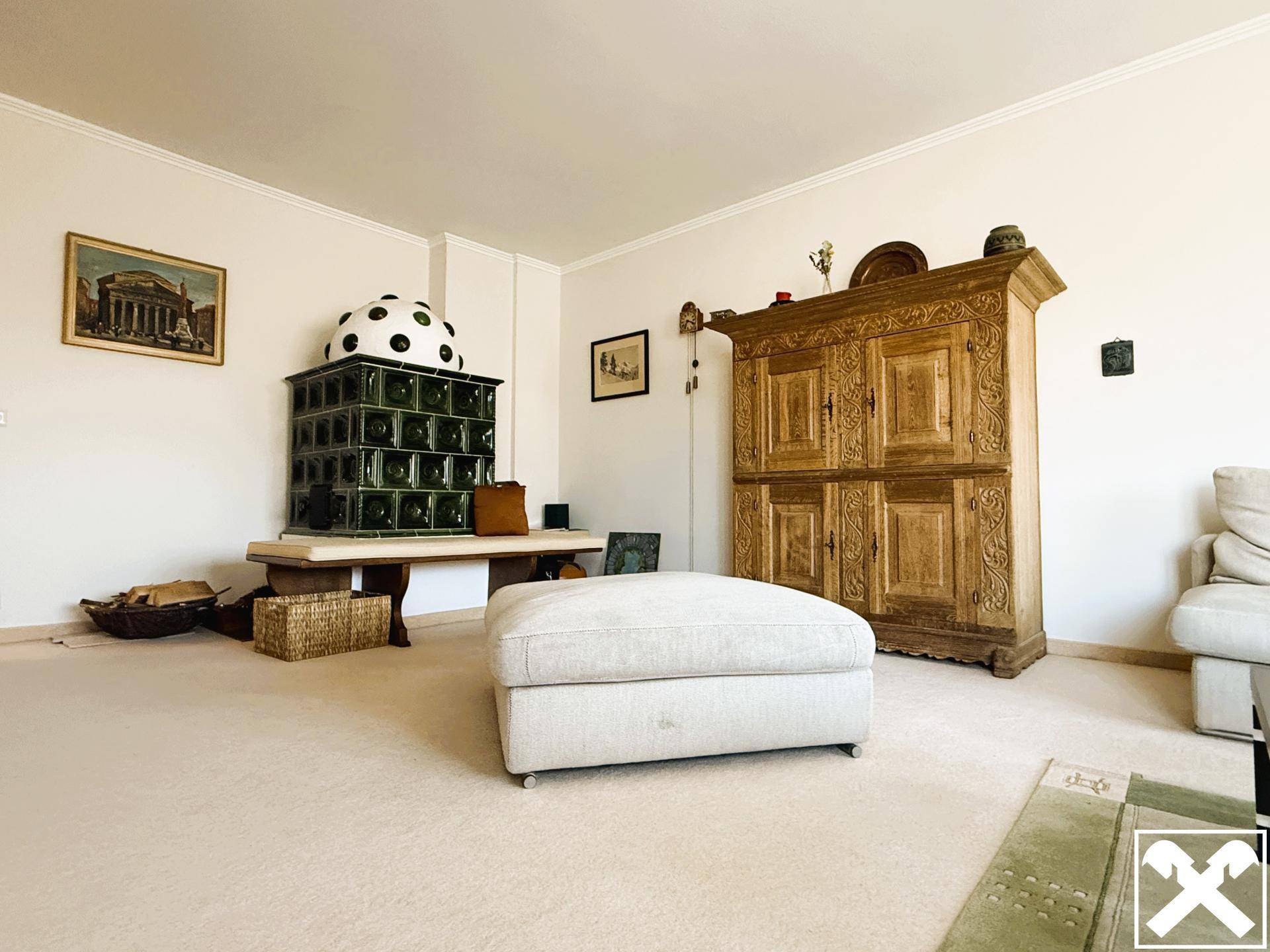 Wohnzimmer mit traditionellem Kachelofen, Teppichboden und rustikalem Holzschrank.