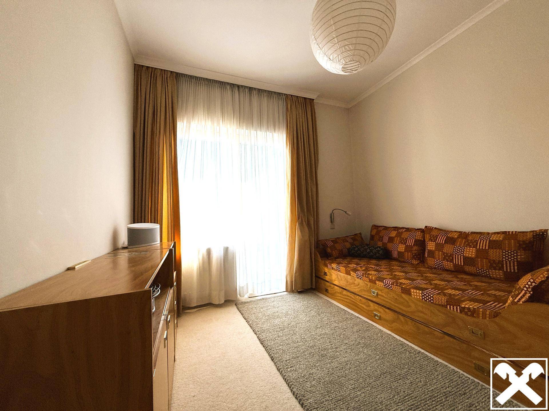 Schlafzimmer mit Tagesbett, Teppichboden und Zugang zu einem Balkon.