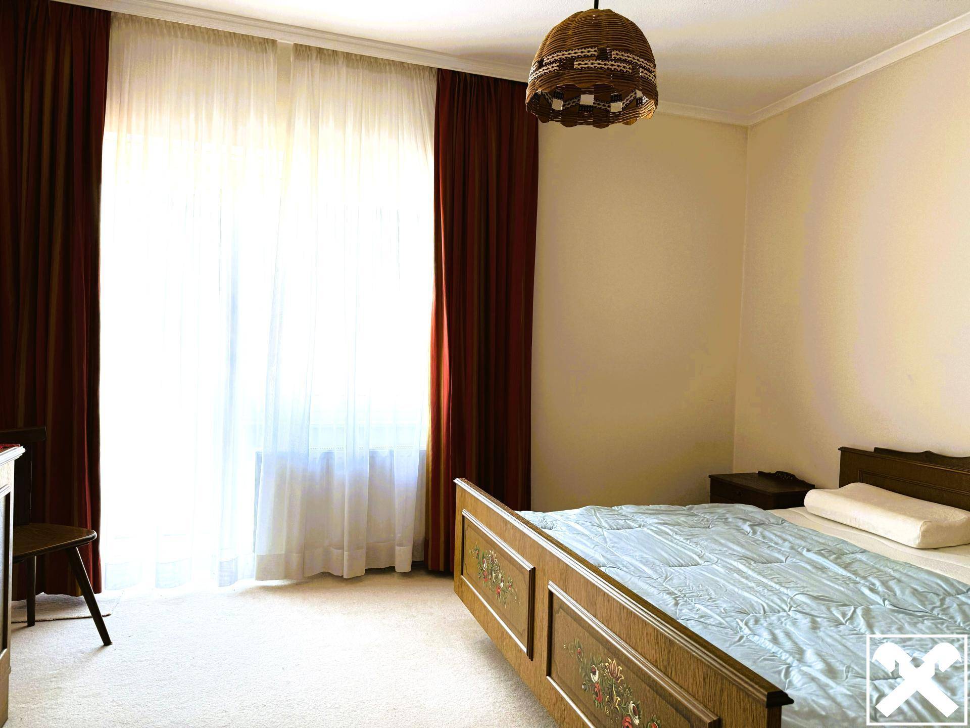 Schlafzimmer mit Doppelbett, Teppichboden und großen Fenstern mit Vorhängen.