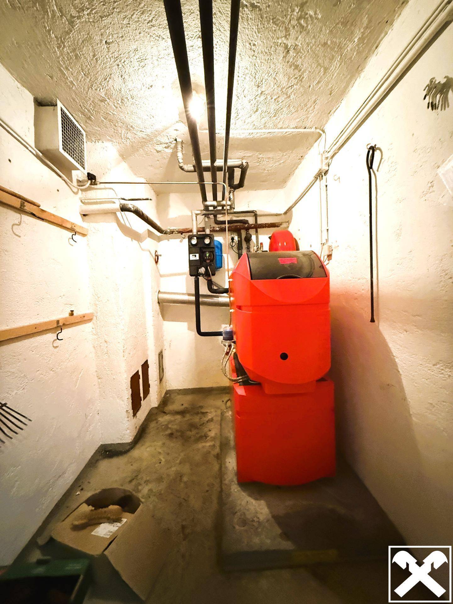 Heizungsanlage mit Rohren und einem großen roten Boiler in einem Technikraum.