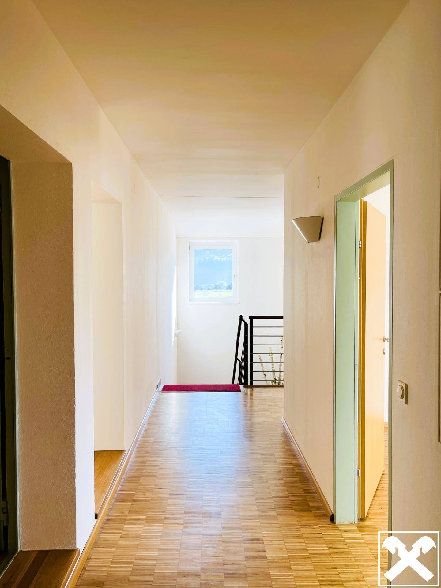Langer, heller Flur mit Holzboden, der zu verschiedenen Büroräumen und einem Treppenhaus führt.