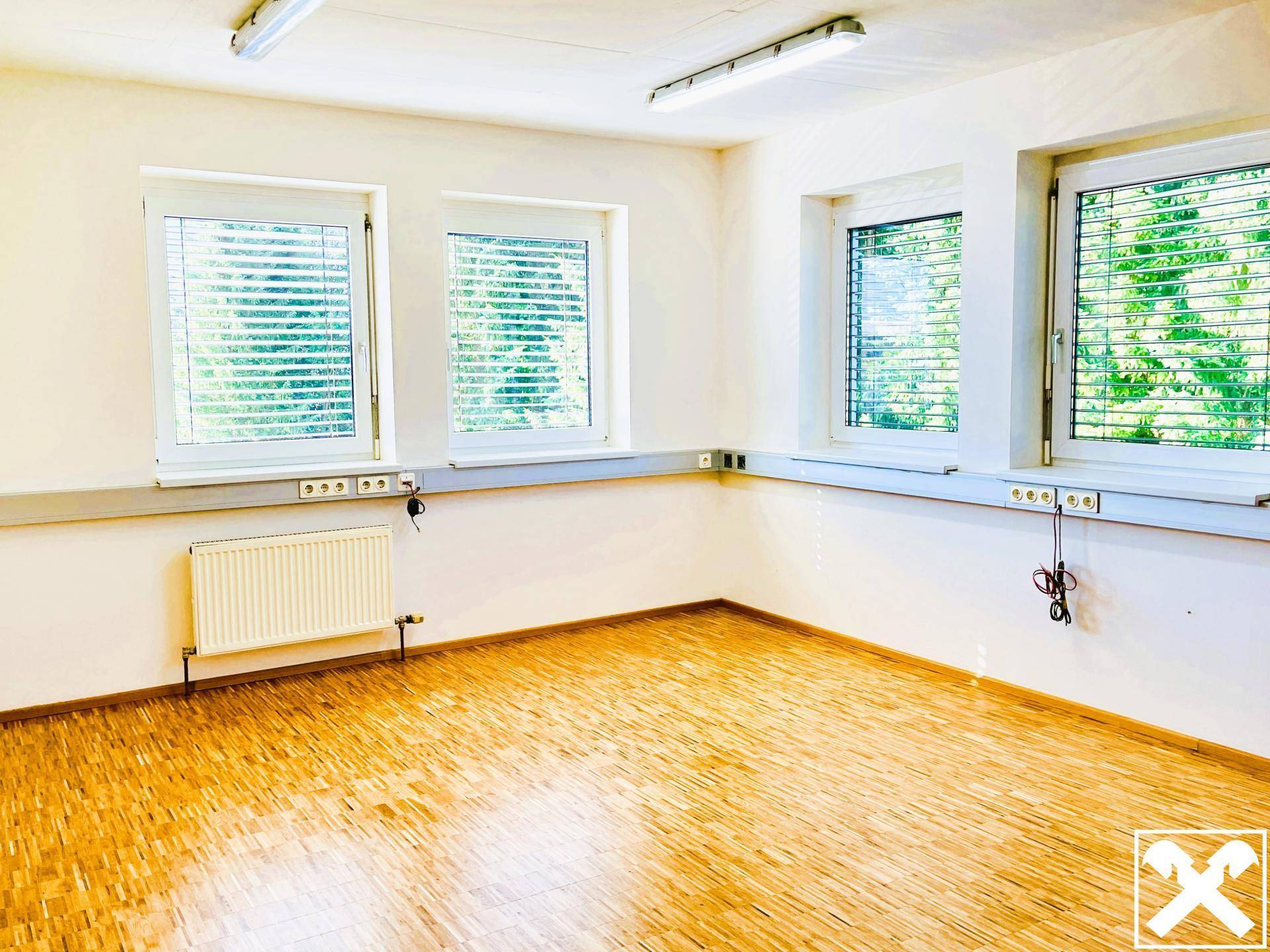 Geräumiges Büro mit Holzboden und mehreren Fenstern, die viel Tageslicht hereinlassen.