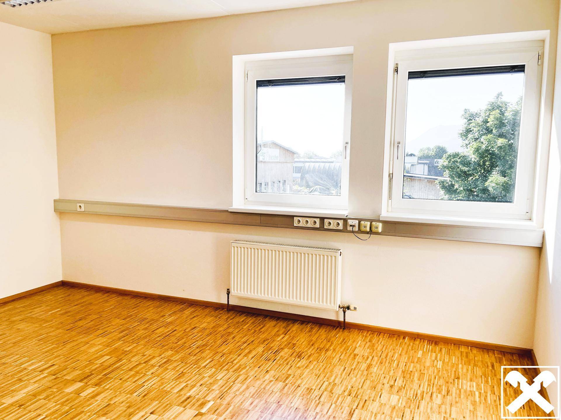 Büro mit Holzboden und zwei großen Fenstern, die einen Blick auf die Umgebung bieten.