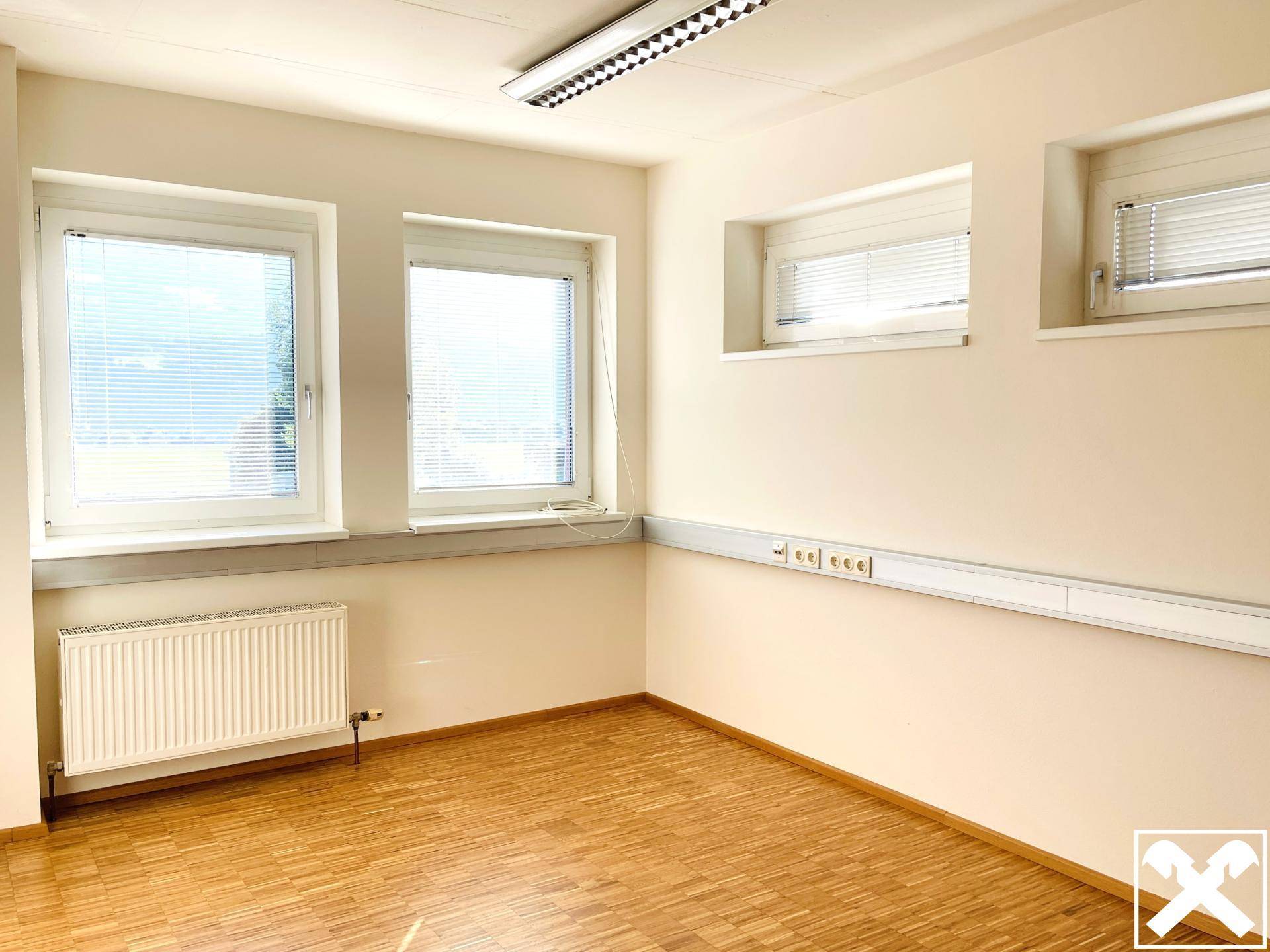 Helles Büro mit Holzboden und mehreren Fenstern, ausgestattet mit Jalousien für Privatsphäre.