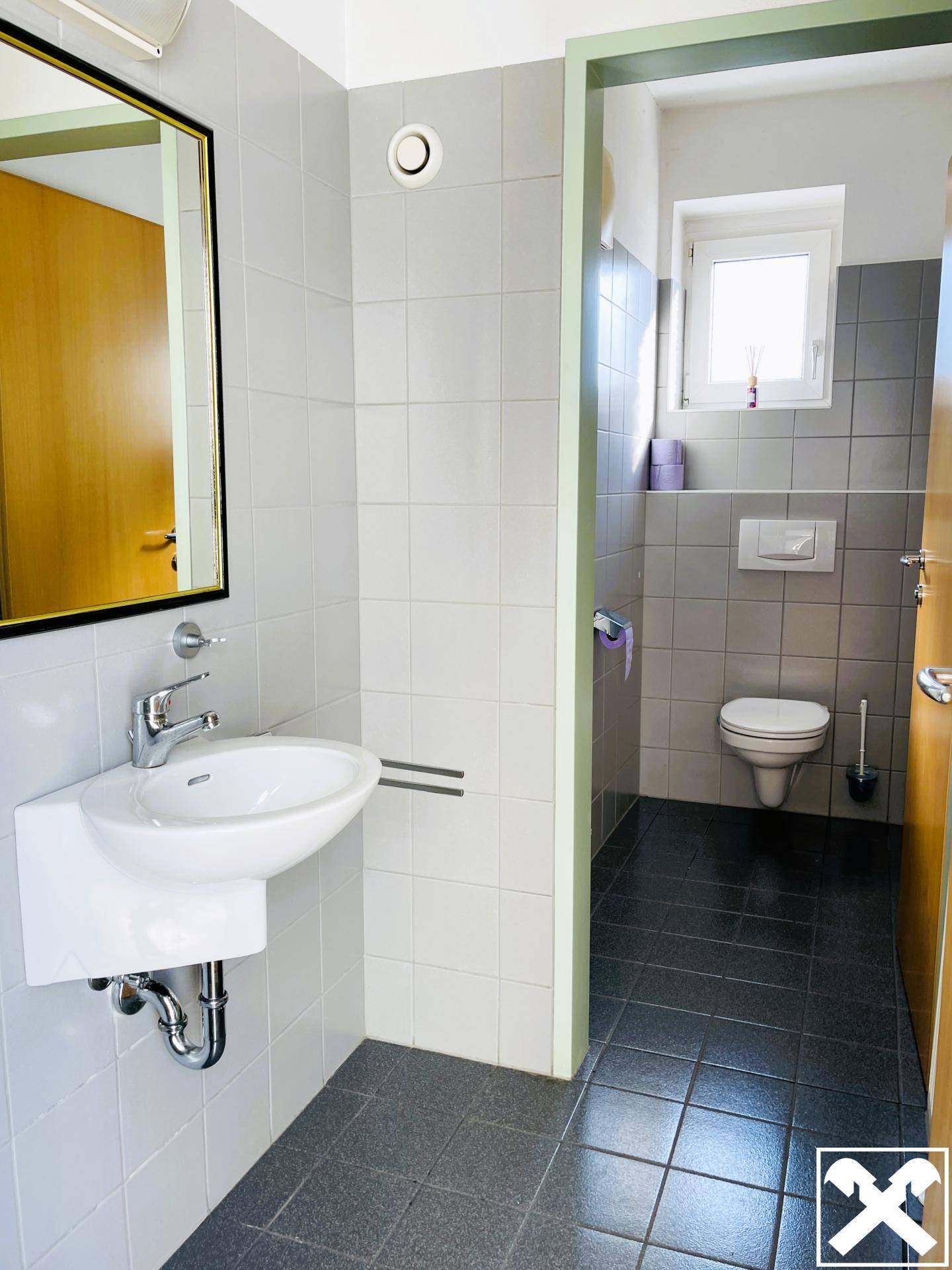Modernes Badezimmer mit Waschbecken, Spiegel und gefliesten Wänden in Grau und Weiß.