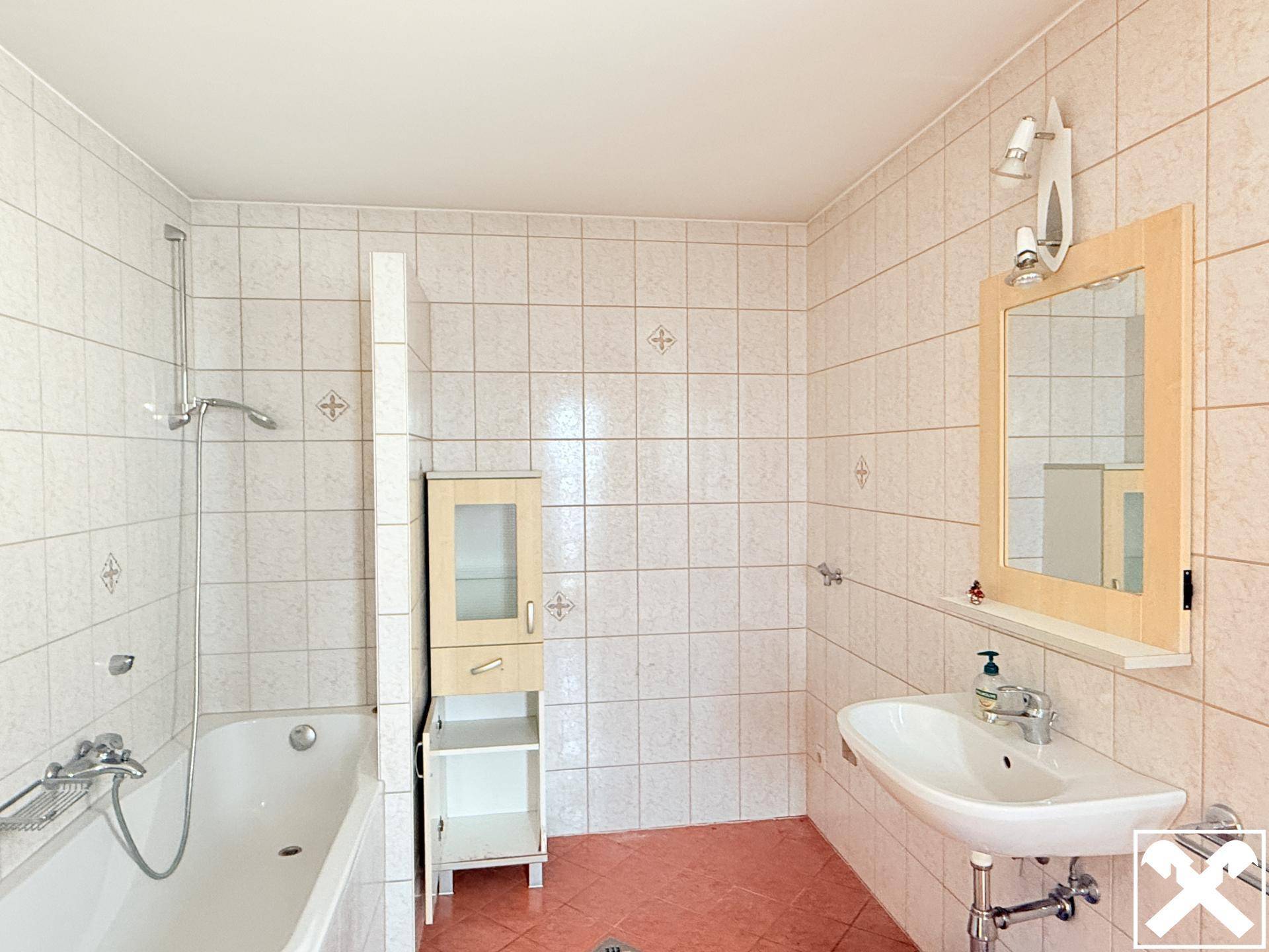 Badezimmer mit rosa Bodenfliesen, weißen Wandfliesen, Badewanne mit Duschfunktion und Einzelwaschbecken.