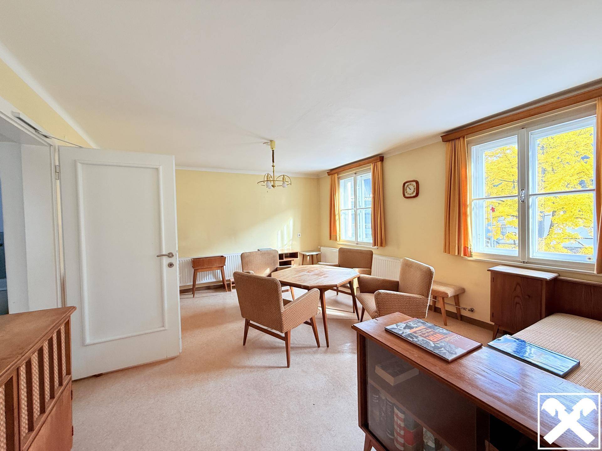 Helles Wohnzimmer mit gelben Wänden, Teppichboden und Vintage-Möbeln, das viel Tageslicht erhält.