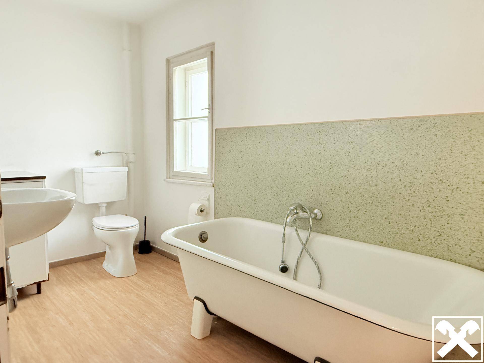 Badezimmer mit weißer und hellgrüner Wand, freistehender Badewanne, Toilette und Einzelwaschbecken.