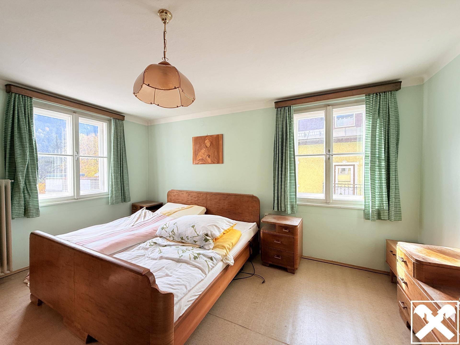 Schlafzimmer mit hellgrünen Wänden, Teppichboden und einem Doppelbett aus Holz, das viel Licht bietet.