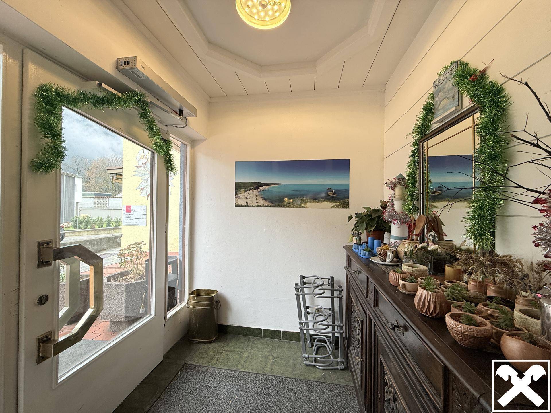 Eingangsbereich mit festlicher Dekoration, gefliestem Boden, großer Glastür und einem Spiegel an der Wand.