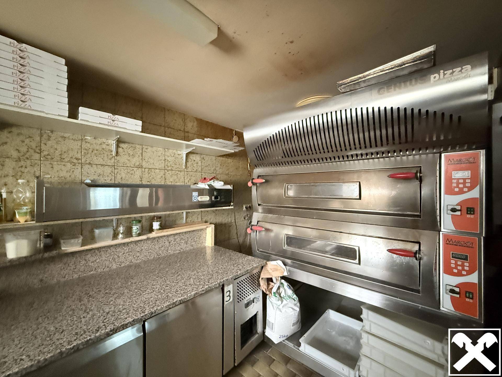 Professionelle Küche mit großen Pizzaöfen, Arbeitsflächen aus Edelstahl und gefliesten Wänden und Böden.