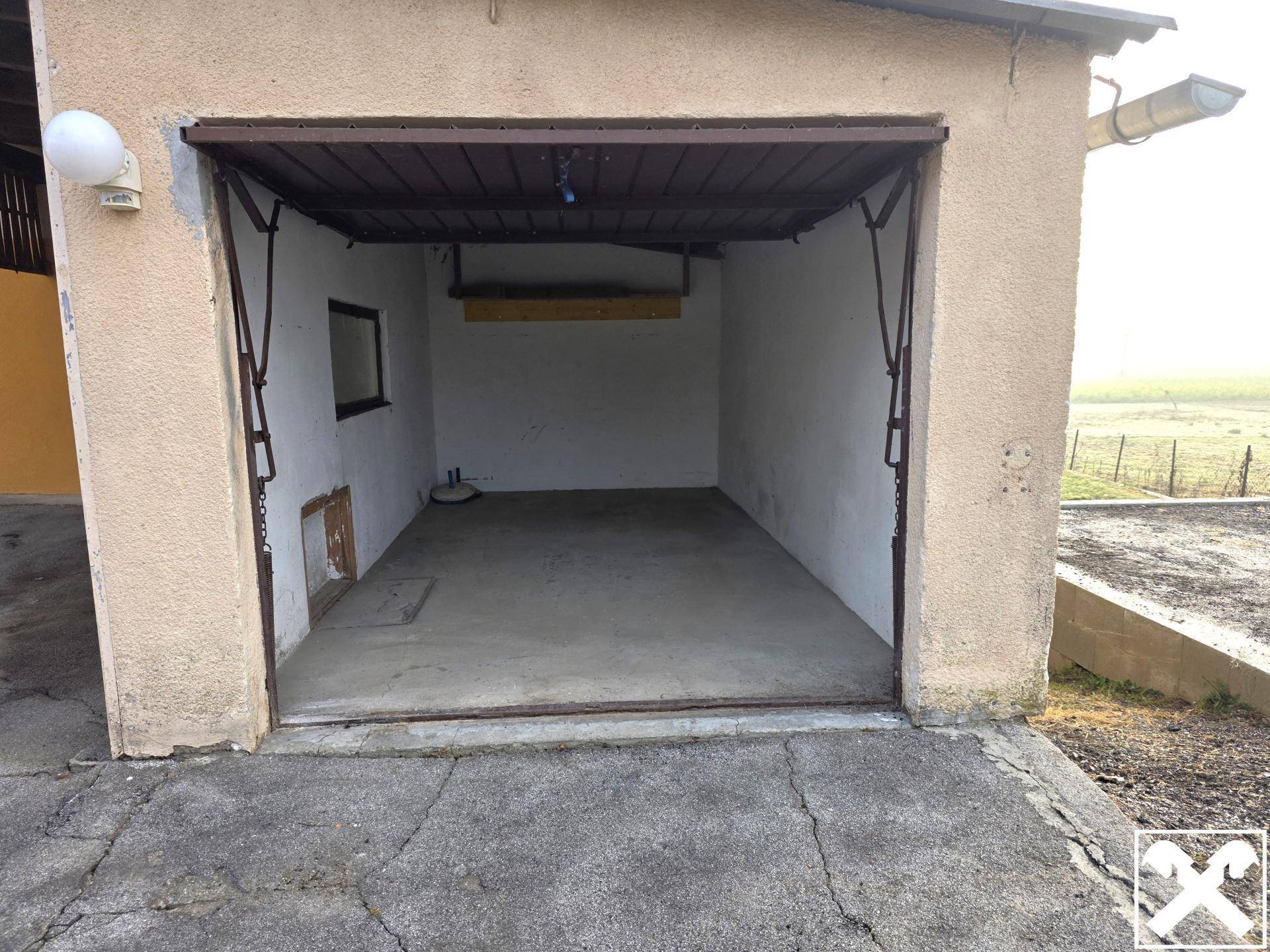 Leere Garage mit Betonboden und einem einfachen Fenster, die Renovierungsbedarf zeigt.