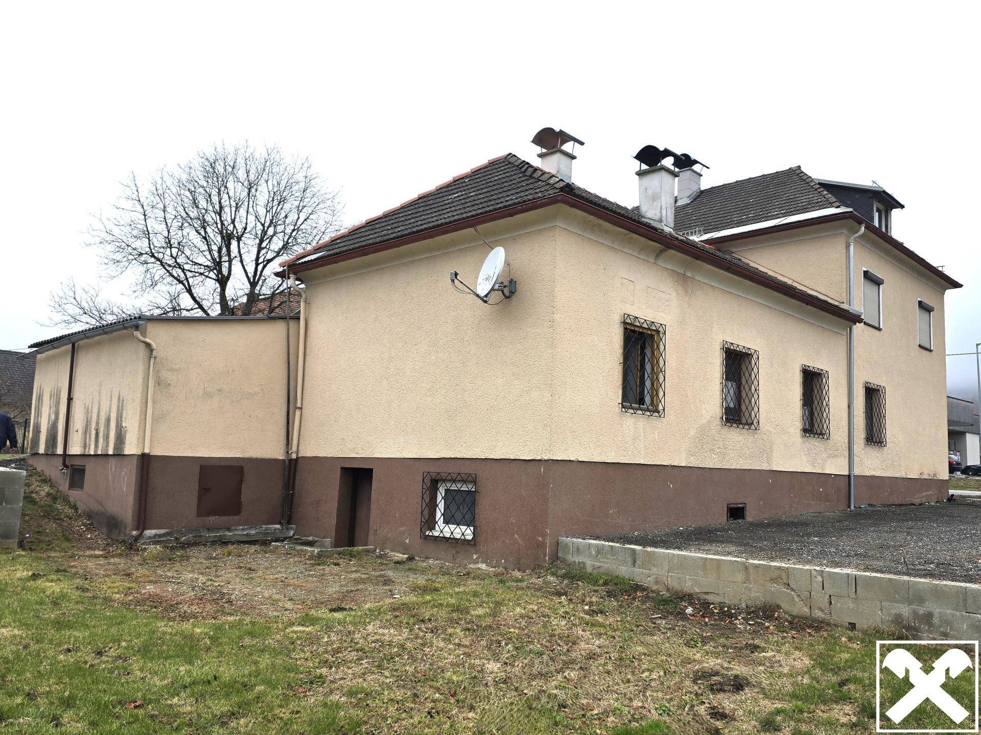 Rückseite des Gebäudes mit einer Rasenfläche und einem Satelliten, die Renovierungsbedarf zeigt.