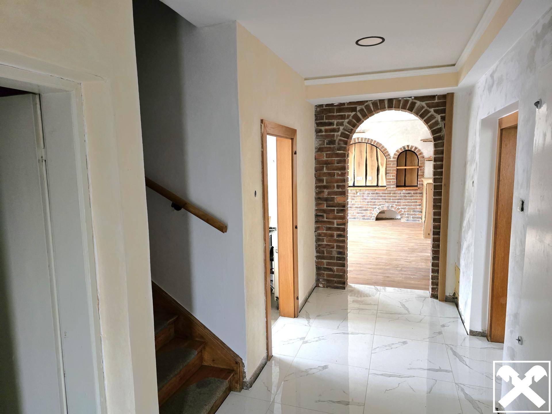 Heller Eingangsbereich mit gefliestem Boden, Holztüren und einem dekorativen Ziegelbogen.