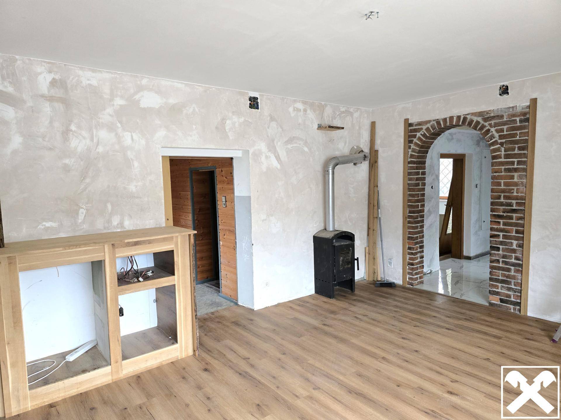 Wohnzimmer mit Holzboden, einem Kaminofen und einem Ziegelbogen, der in einen anderen Raum führt.