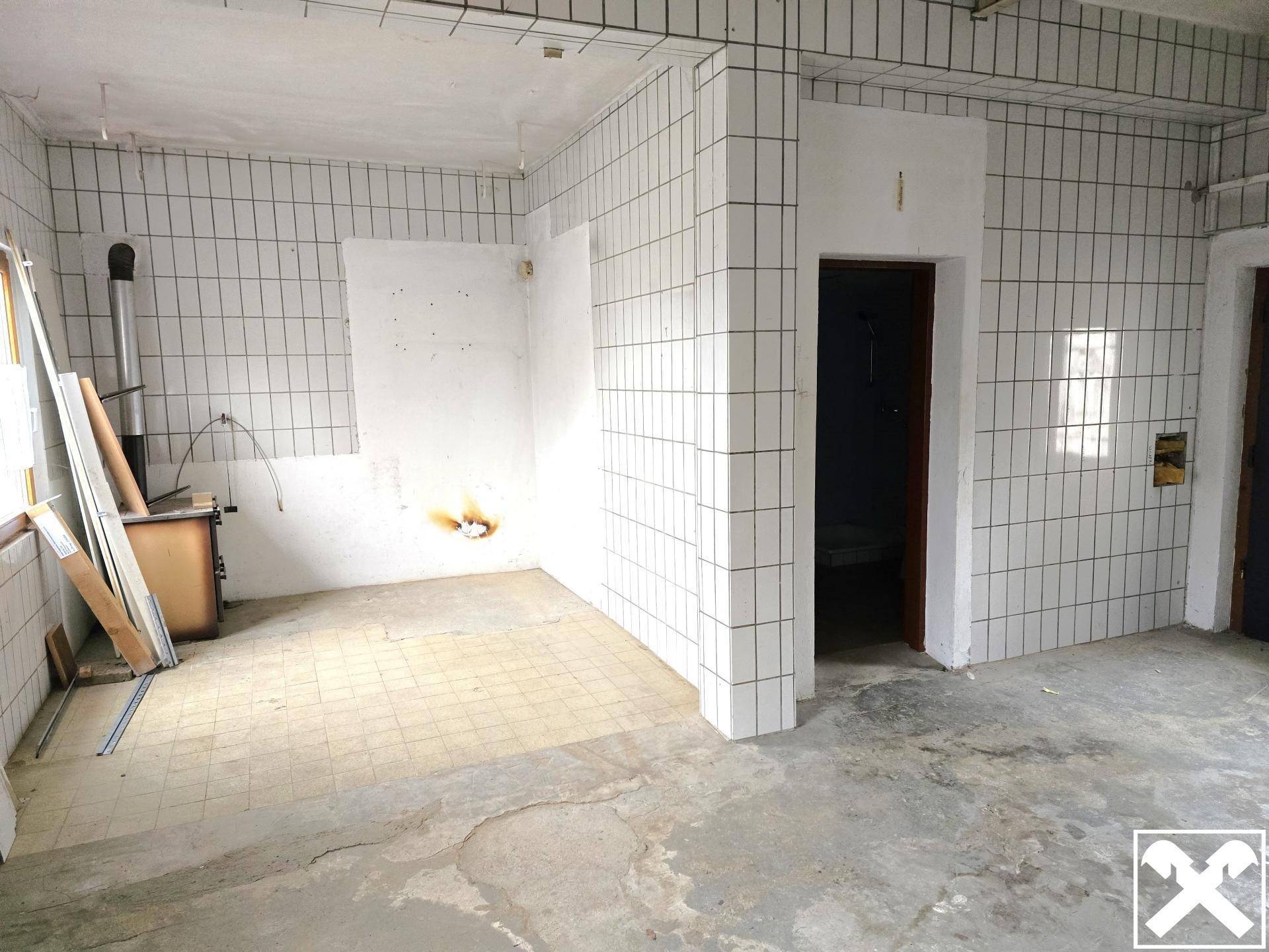 Großer Raum mit weißen Fliesen an den Wänden und einem alten Ofen, bereit für Renovierung.
