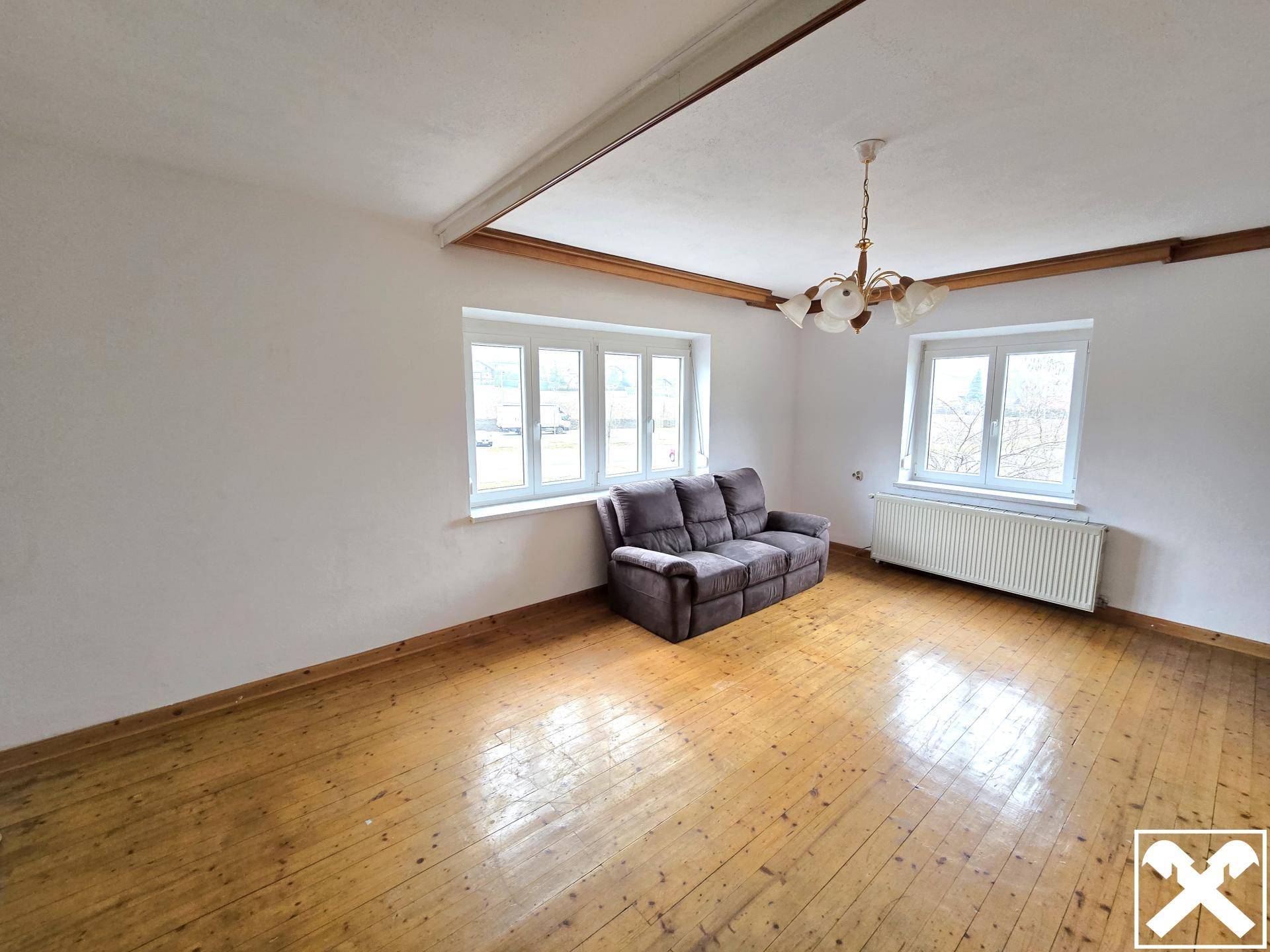 Geräumiges Wohnzimmer mit Holzdielenboden, großen Fenstern und einem bequemen Sofa.