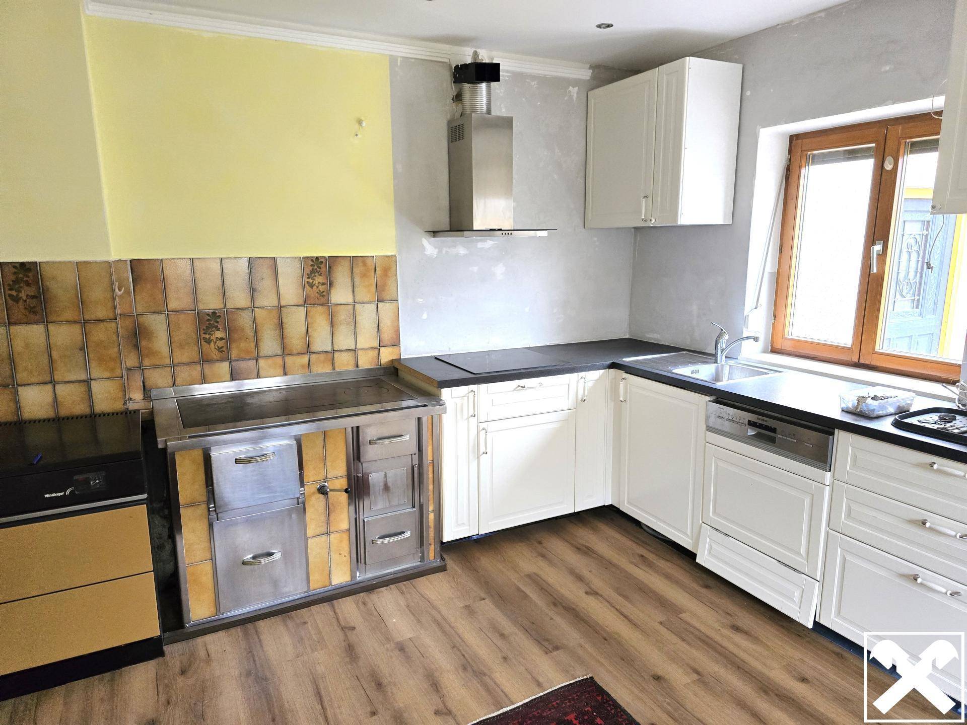 Küche mit weißen Schränken, Holzboden und einem traditionellen Holzofen mit Dunstabzugshaube.