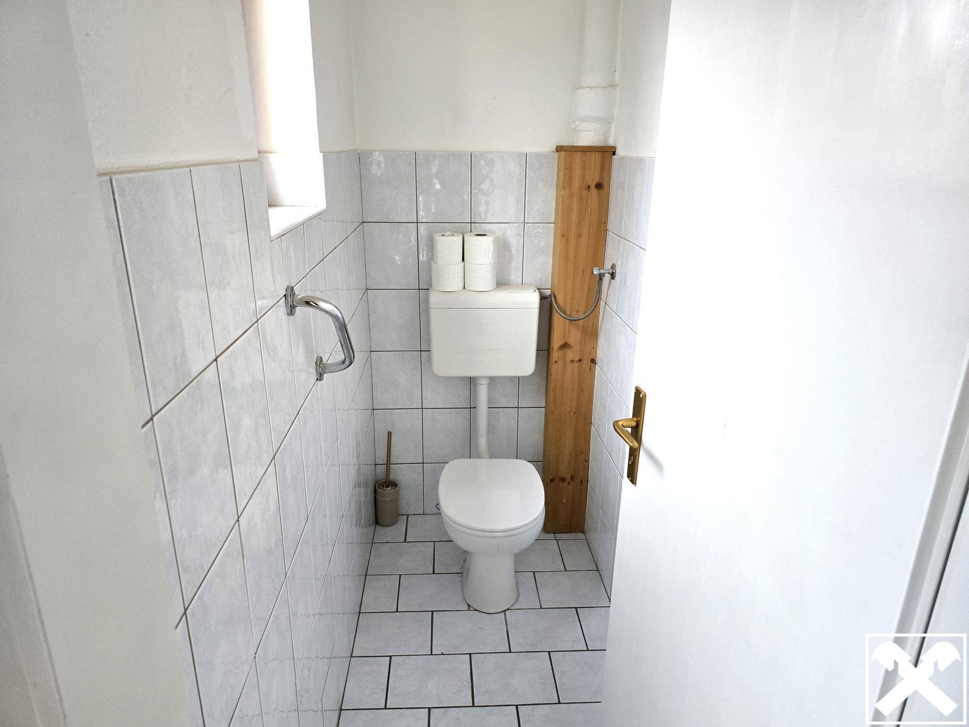Kleines WC mit Fenster, gefliesten Wänden und einem einfachen Stand-WC.