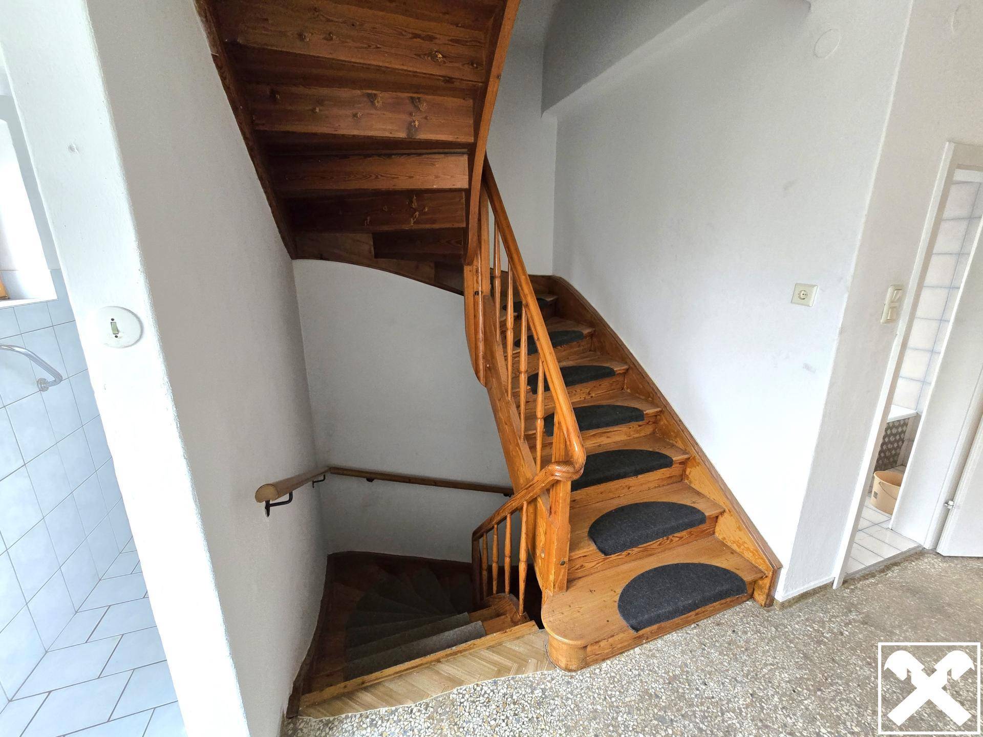 Holztreppe mit Teppichstufen und einem Holzgeländer, die in die oberen Stockwerke führt.