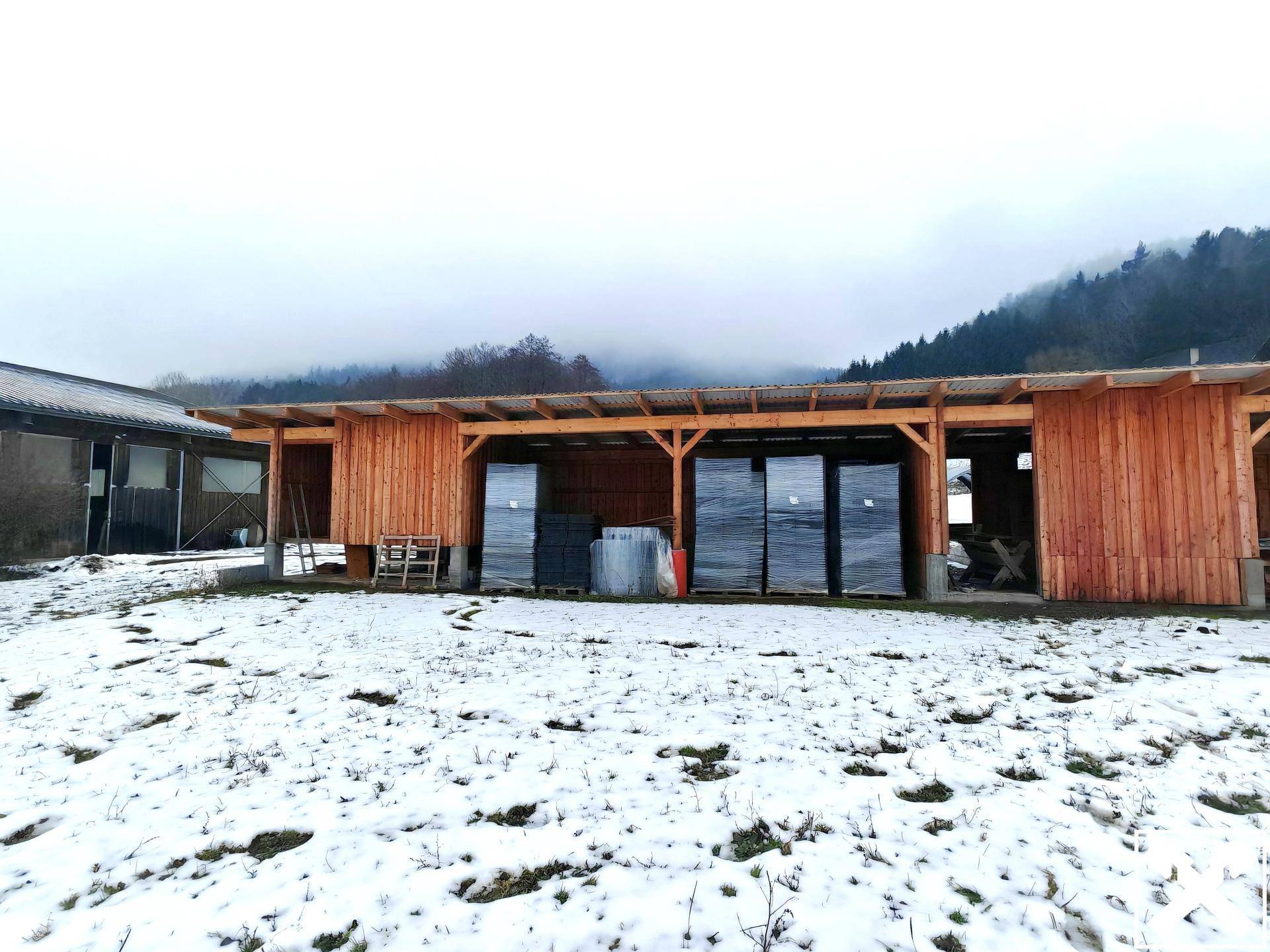 Eine hölzerne Überdachung mit Lagerbereichen und Schnee auf dem Boden, umgeben von Bäumen.