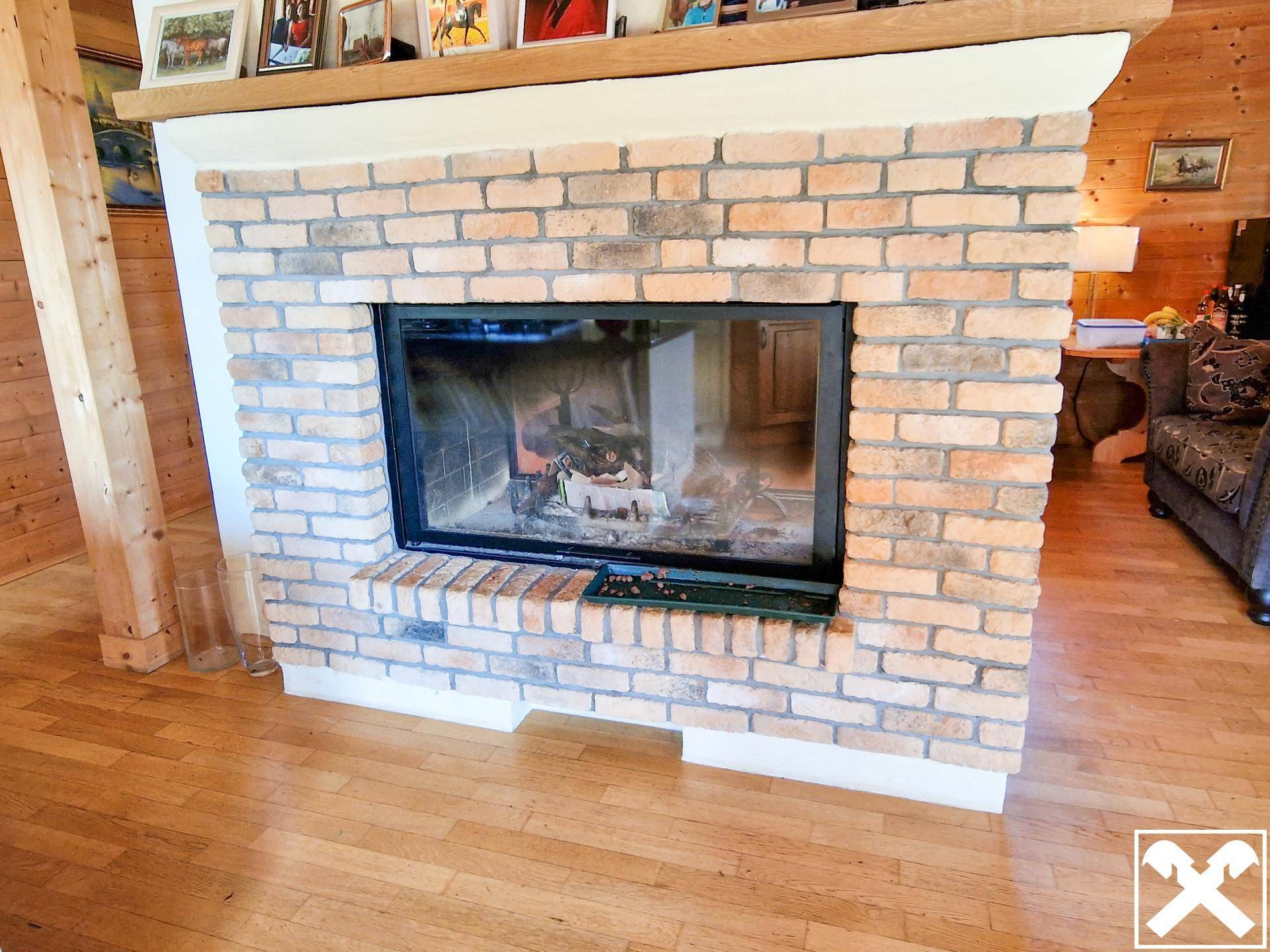 Gemütlicher gemauerter Kamin mit Glasscheibe und Holzfeuer im Wohnbereich.