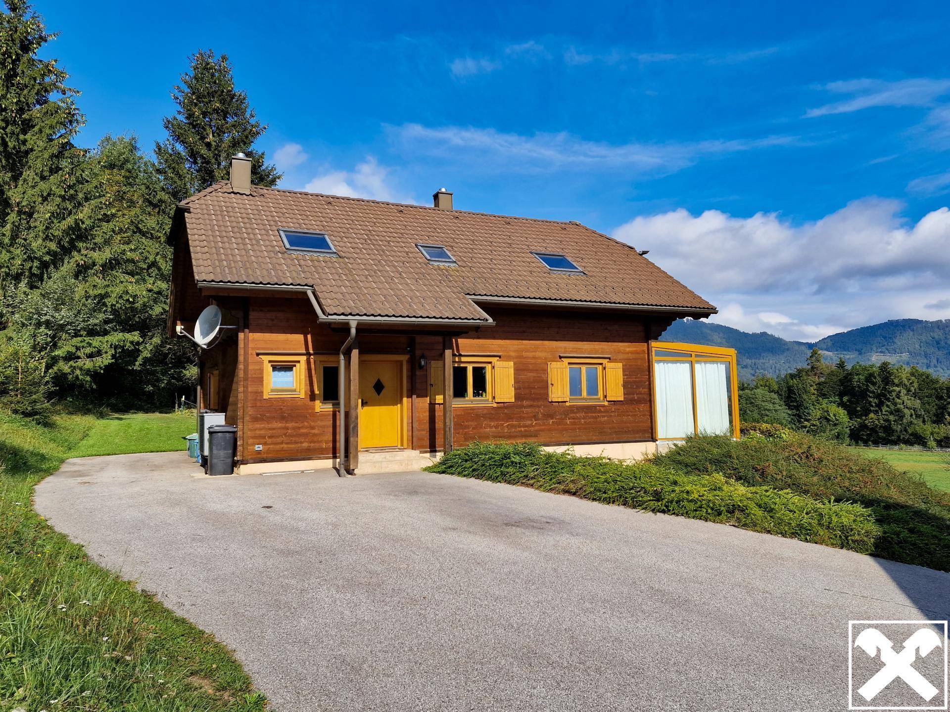 Rustikales Holzhaus mit gelben Fensterläden und weitläufiger Schotterauffahrt im Grünen.