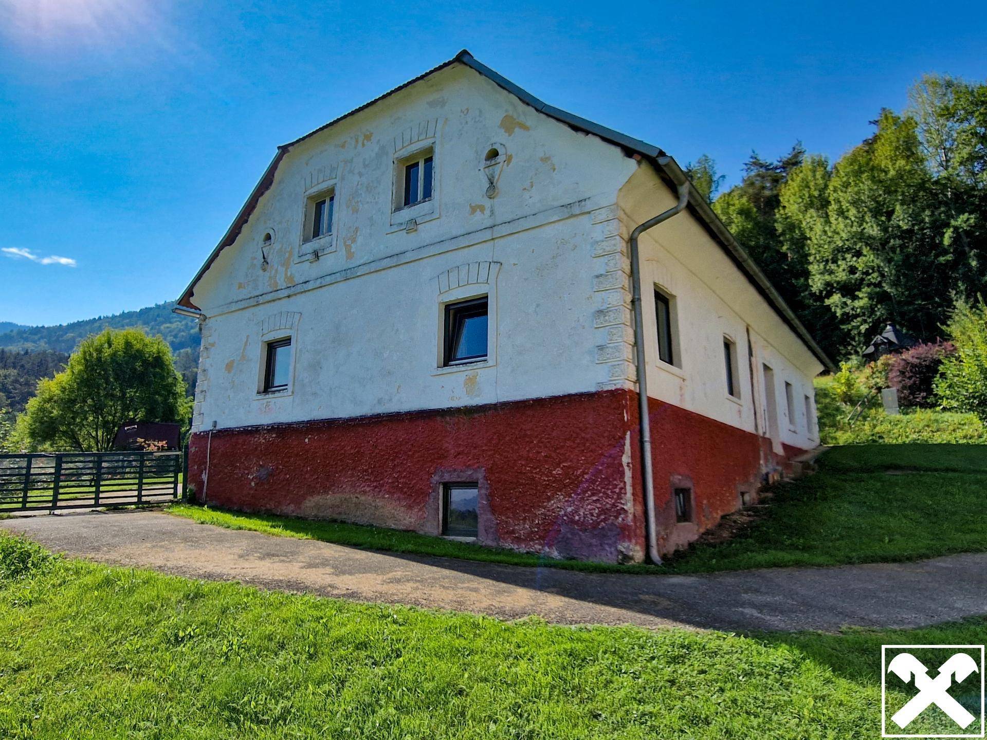Altes Bauernhaus mit weißer und roter Fassade, umgeben von Grün und Bäumen.